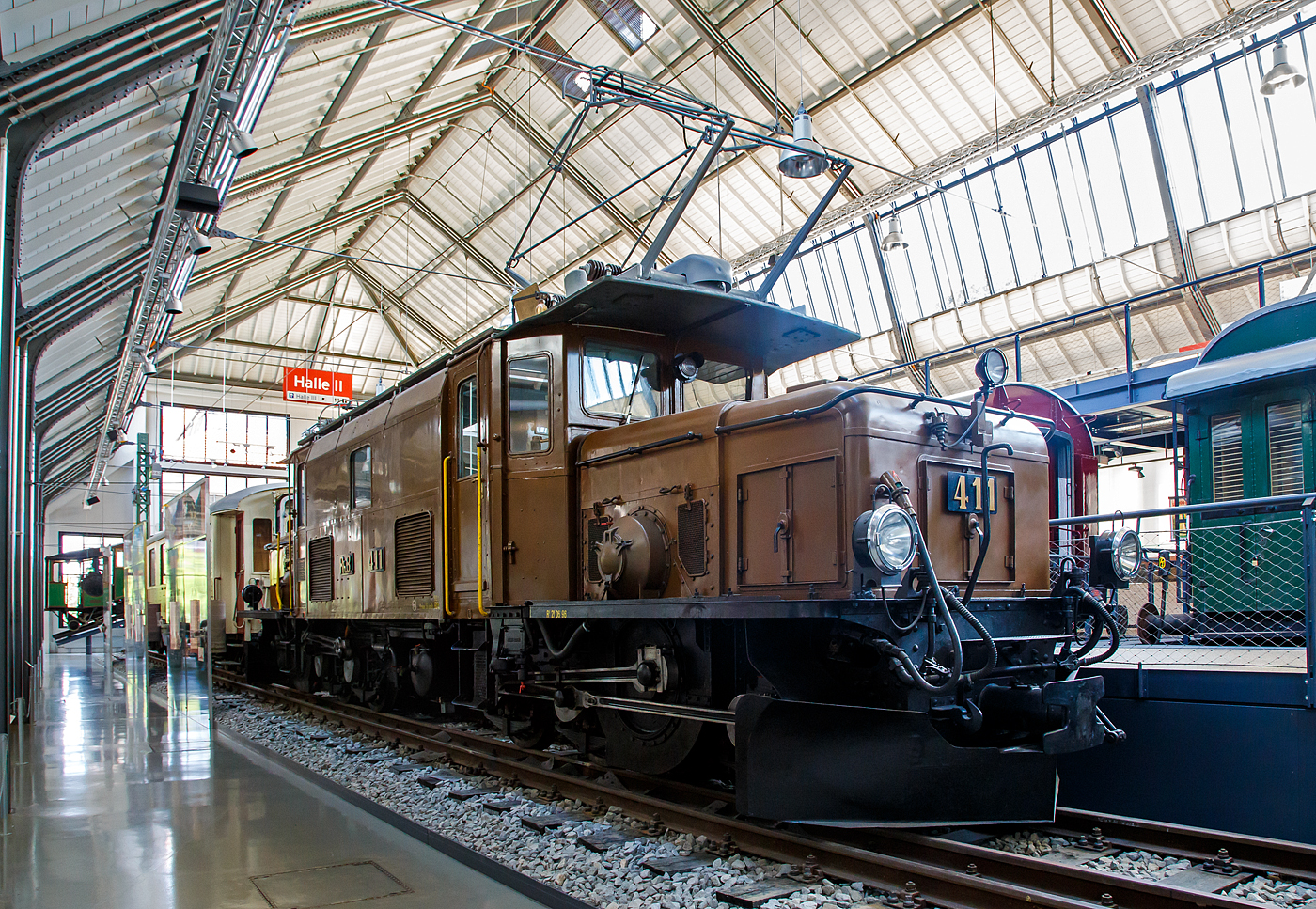 Das Rhätisches Krokodil 411 bzw. die RhB Ge 6/6 I 411, ausgestellt im Verkehrszentrum des Deutschen Museums in München (Theresienhöhe), hier am 16.06.2018.

Die Ge 6/6 I ist eine Elektrolokomotivbaureihe der Rhätischen Bahn (RhB). Wegen ihrer Form und Konstruktion – sie ähneln den SBB-Krokodilen der Gotthardbahn – werden die C'C'-Lokomotiven von Eisenbahnfreunden auch Rhätisches Krokodil genannt, RhB-intern ist C-C die geläufige Bezeichnung.

Die Ge 6/6 I Rh.B. 411 wurde 1925 von A.G. Brown, Boveri & Cie. (Fabrik-Nr. 2241), der Schweizerische Lokomotiv- und Maschinenfabrik Winterthur (Fabrik-Nr. 3344), sowie der Maschinenfabrik Oerlikon gebaut.

Die fortschreitende Elektrifizierung des RhB Stammnetzes mit Einphasenwechselstrom (11 kV, 16 2/3 Hz) zwang die RhB Anfang der 20er Jahre des vergangenen Jahrhunderts zur Beschaffung leistungsfähiger Elektrolokomotiven.
1921 konnten die ersten sechs sechsachsigen Lokomotiven des Typs Ge 6/6 in Betrieb genommen werden. Diese Fahrzeuge, die seinerzeit als die leistungsstärksten Schmalspurlokomotiven der Welt galten, verdrängten schnell die Dampflokomotiven auf der Albulalinie. 1924 konnten vier, 1925 weitere zwei und schließlich 1929 nochmals drei Lokomotiven dieses Types in Dienst gestellt werden.
Mit Auslieferung der Ge 4/4 I und Ge 6/6 II wurden die als Rhätisches Krokodil bekannten Ge 6/6 I in den Güterzugdienst abgeschoben. Dennoch prägten diese Fahrzeuge über Jahrzehnte das Bild der RhB und gelten daher bei vielen Fans noch heute als die RhB-Lokomotive schlechthin.
Erst mit Verfügbarkeit der zweiten Serie der Ge 4/4 II wurde ein Großteil der Krokodile entbehrlich. Nur noch drei Exemplare verblieben auf dem Netz der RhB und stehen noch heute hauptsächlich für Sonderfahrten zur Verfügung.

Das eine oder andere RhB Krokodil blieb der Nachwelt als Denkmallokomotive erhalten. Lok 402 ist seit 1985 im Verkehrshaus der Schweiz in Luzern ausgestellt. Die Nummer 407 stand viele Jahre lang vor einem Zürcher Bankhaus. Sie wurde jedoch wieder nach Graubünden verfrachtet und steht heute auf einem Denkmal in der Nähe des Bahnhofs Bergün. Lok 406 wurde 1984 auf dem ehemaligen ABB Areal in Zürich Oerlikon aufgestellt und später im Werk Pratteln ausgestellt. Dieses äußerlich sehr gut erhaltene Exemplar ist leider nicht der Öffentlichkeit zugänglich. Nummer 413 wurde 1996 verschrottet. Nach einem Rangierunfall wurde die Ge 6/6 411 zusammen mit dem Salonwagen As 1154 im Juni 2001 an das Deutsche Museum in München als Leihgabe abgegeben.

TECHNISCHE DATEN der RhB Ge 6/6 I (Rhätisches Krokodil):
Betriebsnummern: 401 - 415
Hersteller - Kasten und Drehgestelle: SLM
Hersteller - Elektrik: BBC, MFO
Inbetriebsetzung: 1921 - 29
Anzahl Fahrzeuge: 15 (betriebsfähig 2, erhalten 6)
Spurweite: 1.000 mm
Achsanordnung: C'C'
Länge über Puffer: 13.300 mm
Breite: 2.650 mm
Drehzapfenabstand: 5.670 mm
Achsabstand im Drehgestell: 3.275 mm
Triebraddurchmesser (neu): 1.070 mm
Dienstgewicht: 65,9 t
Höchstgeschwindigkeit: 55 km/h
Anzahl Fahrmotoren: 2 vom Typ ELM 86/12
Getriebeübersetzung: 1 : 4,134
Max. Leistung am Rad: 940 kW
Stundenleistung: 794 kW (1076 PS)
Max. Zugkraft am Rad: 195 kN
Dauerzugkraft am Rad: 115 kN
Anhängelast: bei 45 ‰ 160 t / bei 35 ‰ 220 t
Fahrleitungsspannung: 11 kV, AC 16,7 Hz