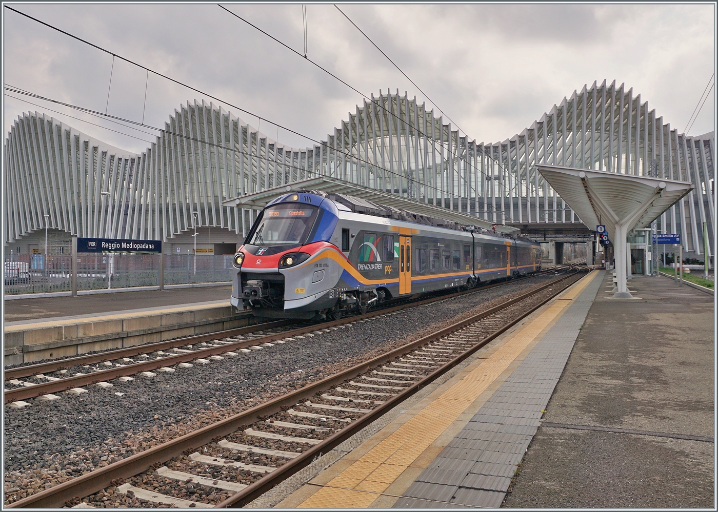 Der FS Treniatalia ETR 103-024 der Tochtergesellschaft TPER (Trasporto Passeggeri Emilia Romagna) ist als Regionalzug 90180 von Reggio Emilia nach Guastalla unterwegs und verlässt den Bahnhof Reggio Mediopadana. Im Hintergrund ist der imposante Bahnhof von Reggio Emilia AV zu erkennen.

14. März 2023