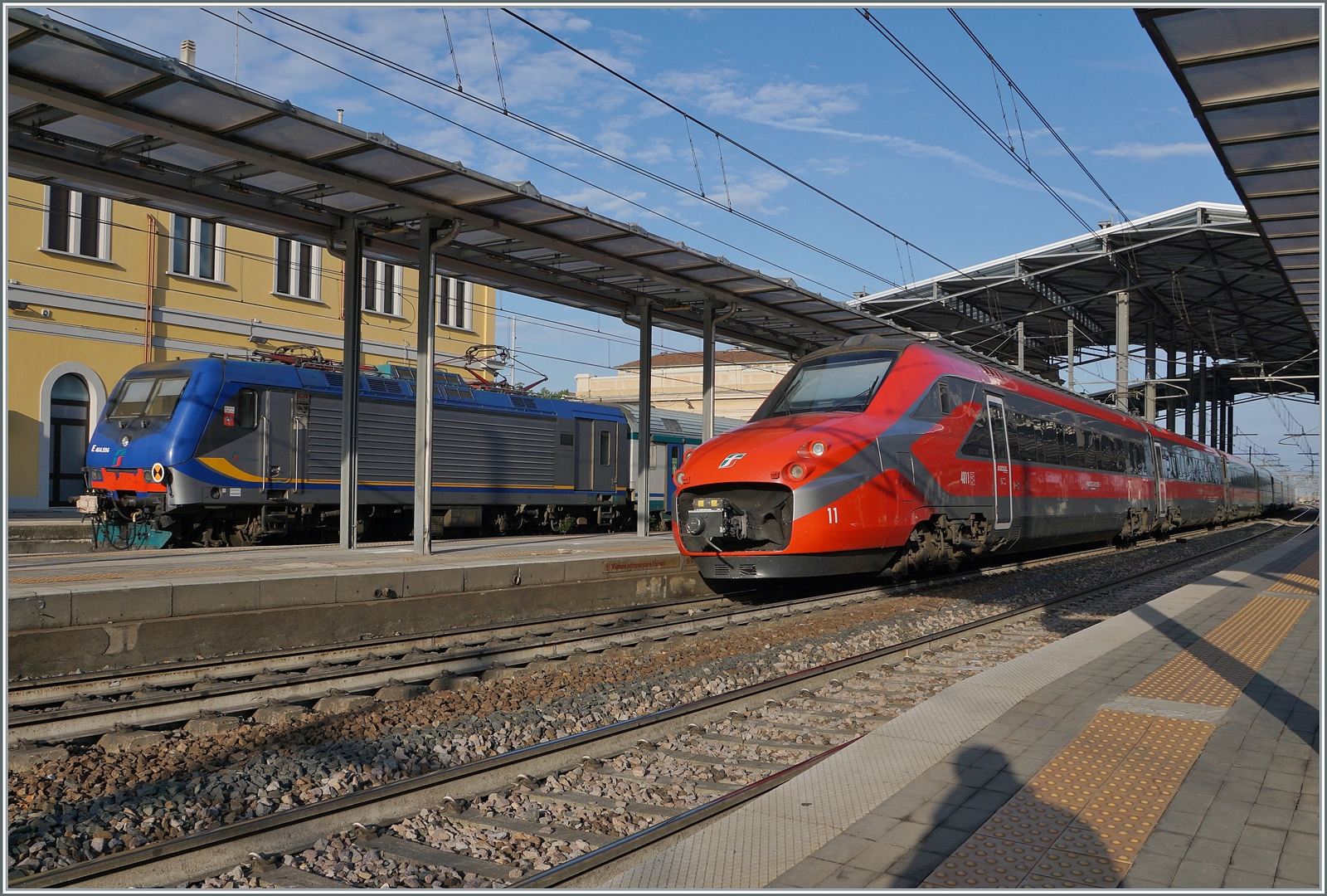Der FS Trenitalia ETR 700 011 (ex Fyra) ist als Frecciarossa 8802 von Ancona nach Milano unterwegs und hat den Bahnhof von Parma erreicht. Links im Bild ist ein FS Trenitala Regionazug von La Spezia in Parma angekommen. 18. April 2023