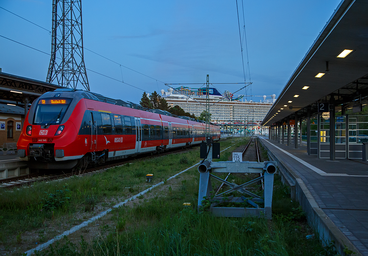 Der fünfteilige Bombardier Talent 2 (442 345 / 442 845) der DB Regio Nordost steht am Abend der 15 Mai 2022 im Bahnhof Warnemünde als S 1 der S-Bahn Rostock nach Rostock Hauptbahnhof zur Abfahrt bereit. Hinten am Pier 8 am Warnemünde Passagierkai liegt das gewaltige Kreuzfahrtschiff NORWEGIAN GETAWAY.