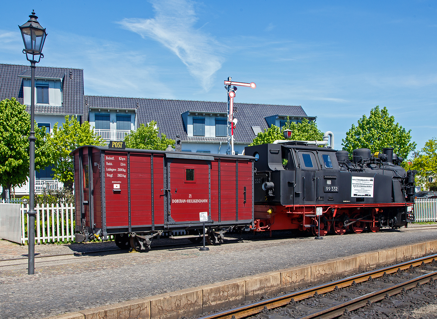 Der historische zweiachsige Postwagen 71 der damaligen DHE - Doberan-Heiligendammer-Eisenbahn (Vorgänger MBB - Mecklenburgischen Bäderbahn Molli), ex DR 98-84-01 ab-/ausgestellt im Bahnhof Ostseebad Kühlungsborn-West (bis 1938 Ostseebad Arendsee), hier am 15.05.2022. Der Wagen ist Eigentum und Leihgabe vom VTM.

Der Post-/ Packwagen wurde 1886 von der Waggonfabrik P. Herbrand & Cie. in Köln-Ehrenfeld gebaut und an die damalige Doberan-Heiligendammer-Eisenbahn (DHE) geliefert. Eine Rekonstruktion erfolgte 2000 – 2001 durch den Verein zur Traditionspflege des Molli e. V..

Die DHE wurde im März 1890 verstaatlichte und in die Großherzoglich Mecklenburgische Friedrich-Franz-Eisenbahn eingliedert. Ab dem 1. April 1920 gehörte sie zur Deutschen Reichsbahn. So kam der Molli nach der deutschen Wiedervereinigung zur DB AG. Zum 01.10.1995 wurde die Mecklenburgische Bäderbahn Molli GmbH gegründet und übernahm fortan die 15,4 km lange Strecke zwischen Kühlungsborn und Bad Doberan von der Deutschen Bahn AG.

TECHNISCH DATEN des Wagens:
Spurweite: 900 mm
Gattung: P
Anzahl der Achsen: 2
Drehzapfenabstand: 2.500 mm
Ladefläche: 8,3 m²
Tragfähigkeit: 2.625 kg

Rechts davor die Molli Museums-/Denkmaldampflok MBB 99 332, eine LKM Typ 225 PS, 900 mm Schmalspurlok, der Mecklenburgischen Bäderbahn Molli GmbH, ex DB 099 905, ex DR 99 2332, ex DR 99 332, ex Wismut 44, am 15.05.2022 beim Bahnhof Ostseebad Kühlungsborn West.

Die 900 mm-Schmalspur-Dampflok der DR-Baureihe 99.33 wurde1951 von LKM (VEB Lokomotivbau Karl Marx Babelsberg) unter der Fabriknummer 30013 gebaut und an die SDAG Wismut (Sowjetisch-Deutsche Aktiengesellschaft Wismut), für die Haldenbahn Oberschlema, (Aue) als Wismut 44 geliefert. Neben zwei weiteren Loks, wurde diese Lokomotive 1958 durch die Deutsche Reichsbahn, für die Bäderbahn Molli, erworben und nach Anpassungsarbeiten im Reichsbahnausbesserungswerk Görlitz als DR 99 332 in Dienst gestellt. Im Jahr 1961 wurden die 99 331 und die 99 332, im RAW Görlitz, auf Heißdampf umgebaut. Die 99 333 blieb eine Nassdampflokomotive und war ab Mitte der 1960er Jahre nur noch Reservemaschine. Mit der Einstellung des Güterverkehrs auf der Strecke wurden nicht mehr so viele Lokomotiven benötigt, so dass diese 1968 ausgemustert wurde.

1970 erfolgte die Umzeichnung in DR 99 2332-7 und 1992 in DR 099 905-2. Nachdem Zusammenschluss beider Deutscher Bahnen zum 01.01.94 wurde sie zur DB 099 905-2. So ging sie zum 01.10.1995, mit der Übernahme des Betriebs auf der Strecke durch die Molli - Mecklenburgische Bäderbahn Molli GmbH, an diese über. Mit der Übernahme wurde auch ein neues Betriebskonzept eingeführt, das die Unterhaltung von zwei noch vorhandenen Lokomotiven der BR 99.33 nicht mehr notwendig machte, so erfolgte zum 07.05.1996 die Außerdienststellung.

Die Schmalspur-Dampf-Lokomotiven des Typs 225 PS Schmalspur des VEB Lokomotivbau Karl Marx wurden basierend auf einem Typenprogramm für kleinere Dampflokomotiven speziell für den Einsatz bei Industriebetrieben entwickelt. Drei dieser Lokomotiven wurden 1958 durch die Deutsche Reichsbahn von der SDAG Wismut erworben. 

Konstruktive Merkmale:
Die Lokomotiven verfügen über einen geschweißten Blechrahmen. Auf dem geschweißten Langkessel sitzt vorn der Dampfdom. Auf dem hinteren Teil sitzen der Sandkasten sowie zwei Kesselsicherheitsventile der Bauart Ackermann. 1961 wurden die 99 331 und die 99 332 auf Heißdampf umgebaut. Dabei erhielten die Kessel jeweils 9 Heiz- und 64 Rauchrohre. Das außen liegende waagerecht angeordnete Zweizylinder-Triebwerk wirkt auf die dritte Kuppelachse. Die außen liegende Heusinger-Steuerung besitzt eine stark vereinfachte Kuhnsche Schleife.

Für die Zugbeleuchtung erhielten die Lokomotiven bei den Anpassungsarbeiten der Deutschen Reichsbahn einen leistungsstärkeren 5 kW Turbogenerator hinter dem Schornstein. Die ursprüngliche Handbremse wurde um eine Knorr-Druckluftbremse ergänzt. Die zweistufige Luftpumpe sitzt rechts neben der Rauchkammer. Die Lokomotiven erhielten wie auf der Bäderbahn üblich ein Knorr-Druckluftläutewerk. Gesandet werden der erste Radsatz von vorn und der letzte Radsatz von hinten.

Für den Einsatz auf der Bäderbahn wurde der obere Teil des Führerhauses stark abgeschrägt, um es an das Lichtraumprofil anzupassen. Das Dach erhielt seitliche Regenrinnen mit Ablaufrohren. Die geschweißten Wasserkästen befinden sich vor dem Führerhaus auf beiden Seiten des Kessels und fassen 3,4 m³. Der Kohlenkasten befindet sich an der Rückwand des Führerhauses und war ursprünglich, da für Braunkohlebrikettfeuerung ausgelegt, mit einem Aufbau vergrößert, der zwischen den beiden Fenstern der Rückwand eingezogen bis auf Höhe des Daches geführt wurde. Er hatte ein Fassungsvermögen von 2,2 t. Da mittlerweile die Feuerung mit Steinkohle erfolgt und bei deren höherem spezifischen Gewicht der Kohlekasten nicht voll gefüllt werden konnte, wurde dieser Aufbau bei 99 2331 bei der Hauptuntersuchung 2004 im Dampflokwerk Meiningen zur Verbesserung der Sicht bei Rückwärtsfahrt entfernt. Sein Fassungsvermögen reduzierte sich dadurch auf 1,5 t. Die, hier gezeigte Museumslok 99 2332 hat noch den ursprünglichen Aufbau.

TECHNISCHE DATEN:
Spurweite: 900 mm 
Achsformel: D h2t
Gattung:  K 44.8
Länge über Kupplung: 8.860 mm
Höhe: 3.490 mm
Achsabstand: 3 x 1.000 mm = 3.000 mm
Leergewicht: 25,0 t
Dienstgewicht: 32,4 t
Höchstgeschwindigkeit: 35 km/h
Indizierte Leistung: 460 PSi
Anfahrzugkraft: 56,39 kN
Kuppelraddurchmesser: 800 mm
Steuerungsart: Heusinger
Zylinderanzahl: 2
Zylinderdurchmesser: 370 mm
Kolbenhub: 400 mm
Kesselüberdruck: 14 bar
Anzahl der Heizrohre:  9
Anzahl der Rauchrohre: 64
Heizrohrlänge: 2.600 mm
Rostfläche: 1,6 m²
Strahlungsheizfläche:  6,04 m²
Rohrheizfläche:  36,85 m²
Strahlungsheizfläche:  6,04 m²
Rohrheizfläche: 36,85 m²
Überhitzerfläche: 18 m²
Verdampfungsheizfläche: 42,89 m²
Wasservorrat: 3,4 m³
Brennstoffvorrat: 2,2 t Kohle
