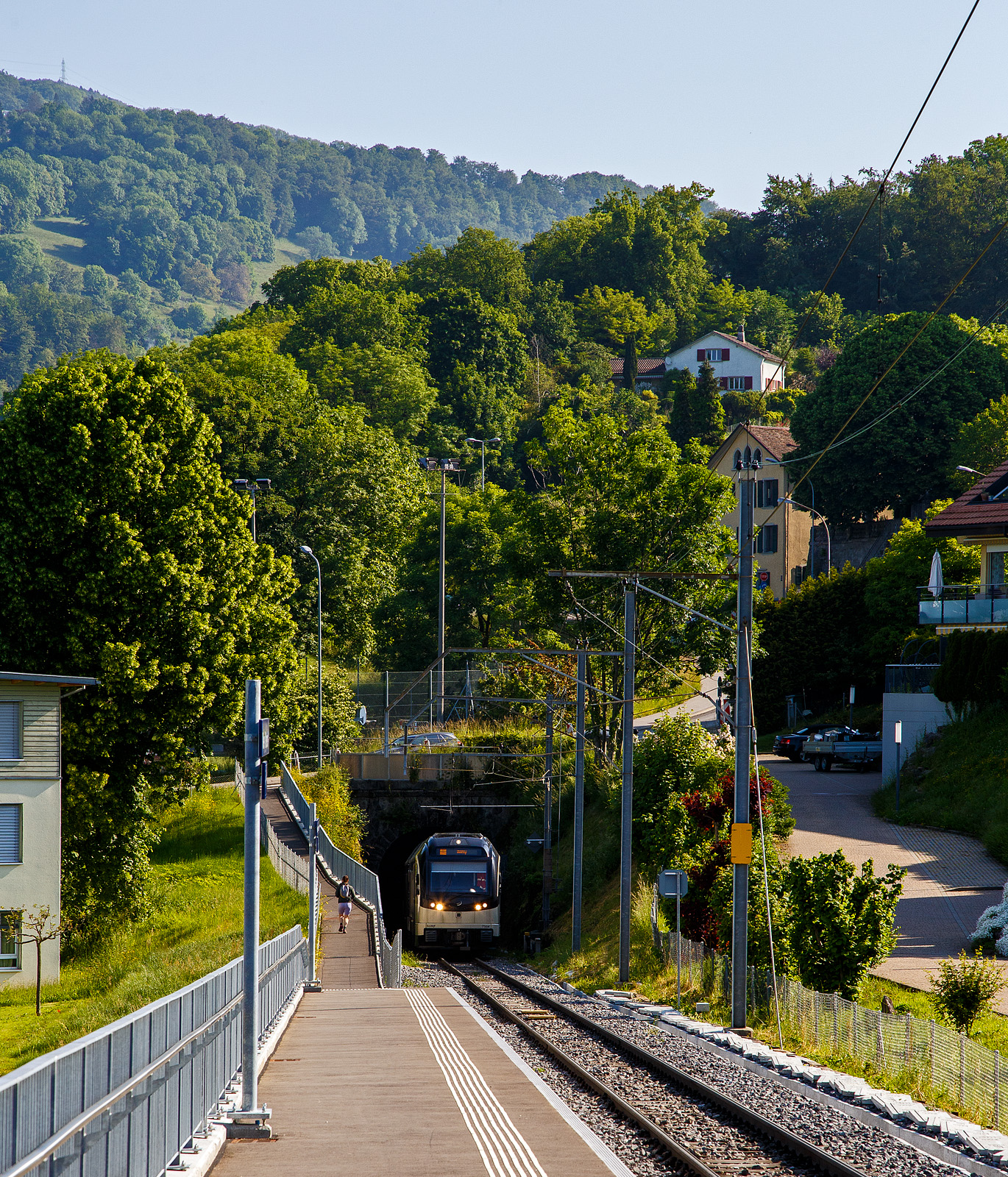 Der MVR (ex CEV) SURF ABeh 2/6 7504  Vevey , als Regionalzug von Vevey nach Blonay, kommt am 27.05.2023 aus dem Tunnel Gilamont und erreicht nun die neue Bedarfshaltestelle Vevey Vignerons. Da wir die Haltewusch-Taste in Richtung Blonay gedrückt haben wird er auch hier halten.

SURF steht für Série Unifiée Romande pour Réseau Ferré métrique (Einheitliche Serie für das Westschweizer Meterspurige Schienennetz). Diese ab 2015 gebaute meterspurige Triebzüge mit gemischtem Adhäsions- und Zahnradbetrieb gehören zu den Stadler GTW der 4. Generation.
