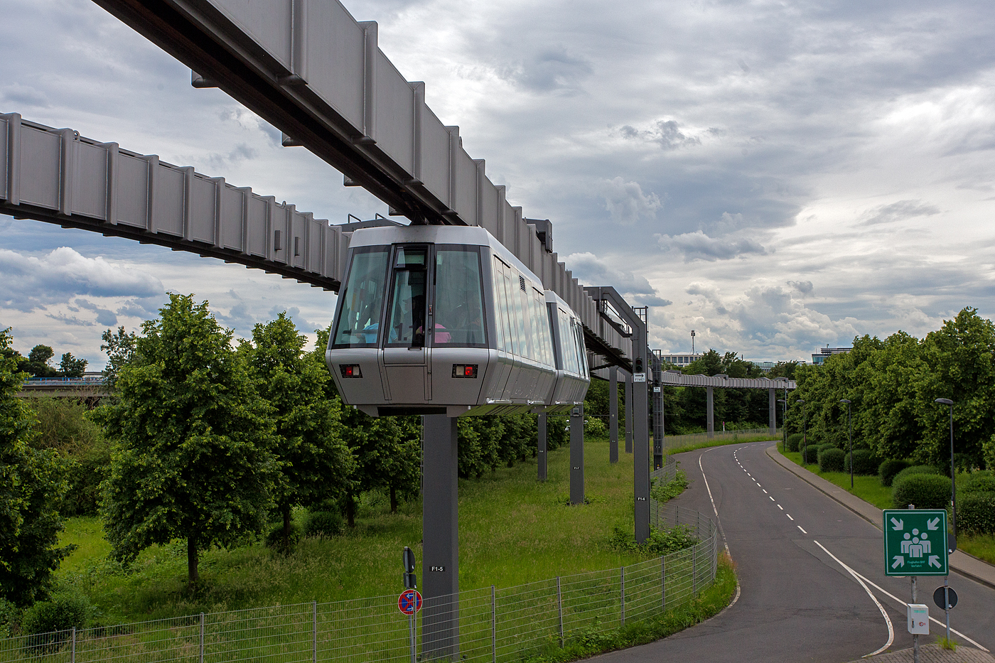 Der SkyTrain Düsseldorf Flughafen, ein Zug (zwei aneinander gekoppelten Kabinen) hat am 26 Mai 2024 die Station Fernbahnhof verlassen und fährt in Richtung Terminal. 

Die vollautomatische Kabinenbahn (fahrerloser Betrieb), die rund 2,5 km lange doppelgleisige Strecke verläuft in etwa 10 Metern Höhe.  Der SkyTrain bringt einen in sieben Minuten (mit bis zu 50 km/h) vom Fernbahnhof zum Terminal. Die Haltestellen sind der Bahnhof Düsseldorf Flughafen, das Parkhaus P4/P5, das Terminal A/B sowie das Terminal C. Die Haltepunkte werden auf Deutsch und Englisch angesagt. Alle Kabinen verfügen über großflächige Panoramafenster und ausreichenden Stauraum für Gepäck. Die Kabinen besitzen außenliegende Schiebetüren und Überstiegstüren an den beiden Stirnseiten.

In Deutschland ist das System der Straßenbahn-Bau- und Betriebsordnung (BOStrab) unterworfen und gilt nach § 4 Abs. 2 PBefG als (vom sonstigen Verkehr) unabhängige Bahn, die dementsprechend auch automatisch, d. h. ohne Fahrpersonal in den Fahrzeugen, betrieben werden darf.

SkyTrain Düsseldorf verfügt über 6 Züge mit je 2 festgekuppelten Kabinen sowie1 Sonderfahrzeug. Die Beförderungskapazität beträgt rund 2.000 Fahrgäste pro Stunde und Richtung, ca. 90 Fahrgäste pro Zug.

Basierend auf der von Siemens Transportation Systems entwickelten Hängebahn-Technologie bestehen die Fahrzeuge aus den Hauptkomponenten Kabine und Fahrwerke.

Eine Kabine ist über vier niveaugeregelte Luftfedern mit hydraulischer Dämpfung an den beiden Fahrwerken befestigt. Die tragende Kabinenstruktur wurde aus hochfesten Aluminium-Strangpreßprofilen aufgebaut, die sich durch hohe Korrosionsfestigkeit und Steifigkeit bei niedrigem Gewicht auszeichnet. Im Inneren der Kabine befinden sich neben 15 Sitz- und 32 Stehplätzen für die Fahrgäste auch alle Betriebsmittel zur Steuerung und Überwachung der Fahrzeugkomponenten. Diese sind in speziellen Geräteschränken untergebracht. Im Bedarfsfall können die Fahrzeuge auch im Handbetrieb mit Fahrern gesteuert werden.

Seit dem 1. Juli 2002 ist der SkyTrain am Flughafen Düsseldorf im Betrieb. Baubeginn war im November 1996. Zuerst wurde der Abschnitt zwischen dem Fernbahnhof und dem Terminal A/B in Betrieb genommen. Diese Strecke ist 2,5 Kilometer lang und weist bis zu 4 % Steigung auf. Der letzte, rund 250 Meter lange Abschnitt bis Terminal C wurde rund 1½ Jahre später mit der Fertigstellung des Terminals eröffnet. Die Baukosten beliefen sich auf rund 150 Millionen Euro, von denen der Flughafen-Bahnhof 35 Millionen Euro verschlang. 62 % der Baukosten wurden durch Fördermittel erbracht.

Auf der Strecke verkehren bis zu sechs Züge aus je zwei aneinander gekoppelten Kabinen, die je 18,4 Meter lang und 2,56 Meter breit sind und mit einer Spannung von 400 Volt betrieben werden. Jeder Zwei-Wagen-Zug bietet 64 Steh- und 30 Sitzplätze. Bei einem Dreiminutentakt befördert die Bahn bis zu 2000 Fahrgäste in der Stunde, jeweils von 3:45 Uhr bis 0:45 Uhr. Die Strecke wird mit einer Reisegeschwindigkeit von 21 km/h im Schnitt in sieben Minuten durchfahren, die Höchstgeschwindigkeit beträgt 50 km/h.

In ihrer Anfangsphase hatte die Bahn mehrfach Probleme mit der sensiblen Auslegung der Sicherheitssysteme, die unbegründete Notbremsungen auf offener Strecke zur Folge hatten. Dies führte phasenweise zur Einstellung des Betriebs. Am 7. Dezember 2006 wurde der SkyTrain vom Flughafen endgültig abgenommen. Nach Aussage des Flughafens wurde vor der Abnahme eine Verfügbarkeit des Systems von über 99 % nachgewiesen. Siemens bleibt Betreiber der Anlage und haftet auch für weitere Ausfälle der Bahn über die Gewährleistungszeit von 25 Jahren.

ANTRIEBSSYSTEM
Die vier Gleichstrommotoren werden über thyristorgesteuerte Stromrichtergeräte betrieben. Die Spannungsversorgung erfolgt mit 400 Volt aus dem Drehstromnetz. Die Bremsenergie wird in das Versorgungsnetz zurückgespeist und damit den anderen Fahrzeugen zur Beschleunigung bzw. zum Fahren zur Verfügung gestellt.

Die von einem Fahrzeug aufgenommene Spitzenleistung beträgt 225 kVA. Die beiden Fahrwerke (einer Kabine) laufen auf 4 gummibandagierten Trag- und Treibrädern in einem kastenförmigen Fahrweg-Träger (einem unten geschlitzten Hohlkastenträger) und werden von 16 Führungsrollen mit Hartgummibandagen (je 4 Doppelrollen vorne und hinten) geführt und somit in der Spur halten. Es ist damit wesentlich komplexer aufgebaut als ein Fahrwerk der Wuppertaler Schwebebahn, das aus lediglich 2 Rädern besteht. Im Innern des Fahrbahnträgers (Hohlkastenträger) laufen die Fahrwerke weitgehend witterungsgeschützt, zudem sind so die Führung und Stromversorgung wettergeschützt.Das Antriebssystem eines Fahrzeuges besteht aus zwei weitestgehend unabhängigen, redundanten Einheiten, die wiederum über je zwei parallelgeschaltete Fahrmotoren verfügen. Beim Ausfall eines Systems kann die Fahrt also bis zur Endhaltestelle fortgesetzt werden.

Die Stromabnahme läuft über vier seitlich angebrachte Stromschienen, dabei wird Dreiphasenwechselstrom (Drehstrom) mit einer Spannung von 400 Volt übertragen, der ohne Umformer und eigene Umspannstationen direkt aus dem Drehstromnetz genommen wird. Darüber liegen Linienleiter zur drahtlosen Übertragung von Daten zwischen Fahrzeug und Leitstand.

Weichen ermöglichen Verzweigungen des Fahrwegs. Bahnsteigtüren verhindern Abstürze aus hoch gelegenen Bahnhöfen bzw. ein Betreten der Gleisbereiche.

Die H-Bahn wird von einer zentralen Leitstelle aus überwacht und kommt so ohne Fahrpersonal in den Zügen aus. Sie könnte auch je nach Auslastung, im Takt- oder im Rufbetrieb eingesetzt werden, wobei im letzteren der Fahrgast sich die Kabine wie einen Personenaufzug per Knopfdruck „bestellt“.

TECHNISCHE DATEN DES ANTRIEBS: 
Fahrspannung: 3 x 400 V, 50 Hz
Nennleistung Fahrmotoren: 4 x 31,5 kW
Drehzahlbereich: 0..3290 U/min
Nenndrehmoment:  4 x 90 Nm
Antriebskraft (Nennwert): 8,4 kN
Antriebskraft (Anfahrzugkraft): 16,8 kN
betriebliche Beschleunigung: 1 m/s²
betriebliche Verzögerung: 1 m/s²
Sicherheitstechnische Verzögerung: > 1,5 m/s²
Höchstgeschwindigkeit: 13,9 m/s (50 km/h)
Positioniergenauigkeit: ± 3 cm
Fahrgeräusch (bei 50 km/h in 25 m Entfernung) < 65 dB/A

TECHNISCHE DATEN einer Kabine:
Länge über Kupplungen:  9.200 mm
Länge der Kabine: 8.232 mm
Breite der Kabine: 2.244 mm
Höhe der Kabine: 2.623 mm
Lichte Weite eine Fahrgasttür: 1.350 mm (2x je Längsseite einer Kabine)
Mittenabstand Fahrgasttüren: 4.600 mm
Mittenabstand Fahrwerke: 5.689 mm
Gewicht eines Fahrwerks: 1.750 kg
Leergewicht einer Kabine : 4.955 kg
Leergewicht Fahrzeug: 8.455 kg (1 Kabine mit 2 Fahrwerken)
Zuladung (nach BOStrab): 4.923 kg
zulässiges Gesamtgewicht: 13.378 kg
Sitzplätze: 15
Stehplatze: 32
