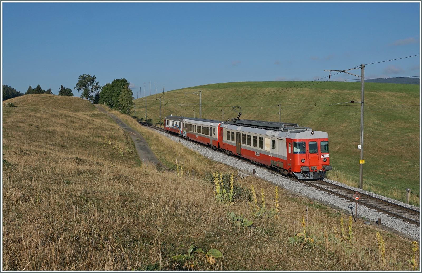 Der sogenannte  Schülerzug , bestehend aus dem ABt 375 (ABt 50 85 80 33 325-7), dem B 536 (B 50 85 2035 536-5 CH-TVYS) und dem TRAVYS RBDe 567 174 (94 85 7567 174-8)  Fleurier , ist als Regionalzug 6009 von Vallorbe nach Le Brassus kurz nach Les Charbonnières unterwegs. 

Es ist einer der letzten Planmässigen Einsätze des Zuges, mit dem neuen Fahrplankonzept der PBr wurde die Komposition überflussig.
Leider war der ABt und der B bereits verschmiert, das  Gesamtwerk  wurde aber durch die Bildbearbeitung seiner Aussagekraft beraubt. 

21. Juli 2022 