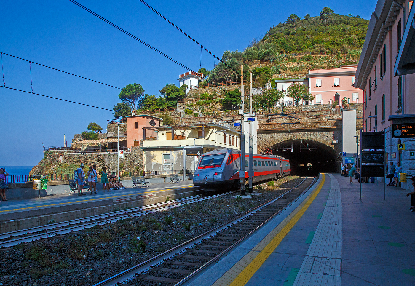 Der Trenitalia Frecciargento ETR 485 - 34 (Pendolino) fährt am 22.07.2022 durch den Bahnhof Riomaggiore in Richtung Genova.

Riomaggiore ist das südlichste der fünf Dörfer der Cinque Terre (Fünf Ortschaften) und verfügt, wie die anderen Dörfer, über einen Bahnhof an der Bahnstrecke Pisa–Genua (RFI Strecke-Nr. 77 / KBS 31 La Spezia–Genua), die den Ort mit den Nachbardörfern und mit La Spezia und Levanto verbindet. Der Bahnhof von Riomaggiore liegt am nordwestlichen Ortsrand, nur drei bis vier Wagenlängen befinden sich unter freiem Himmel, der Rest der Bahnsteige ist in den beiden Tunneln (davor und dahinter). Der Ortskern wird mittels eines in einem Eisenbahntunnel verlaufenden Fußpfades angebunden.

Hier mit Blick auf den nördlichen Tunnel (in Richtung Levanto). Rechts das Empfangsgebäude. Rechts und links vom Tunnelportal die Aufzüge (Lifte) vom einen zum anderen Bahnsteig für den barrierefreien Übergang. Es gibt auch eine Unterführung mit Treppen. 

Man kann auch mit dem Lift über den Tunnel fahren und geht dann nach links wo dann die Via dell'Amore beginnt. Dies ist ein in den Fels gehauener Fußweg zum nahe gelegenen Manarola, mit malerischen Aussichten (gegenwärtig aber gesperrt).