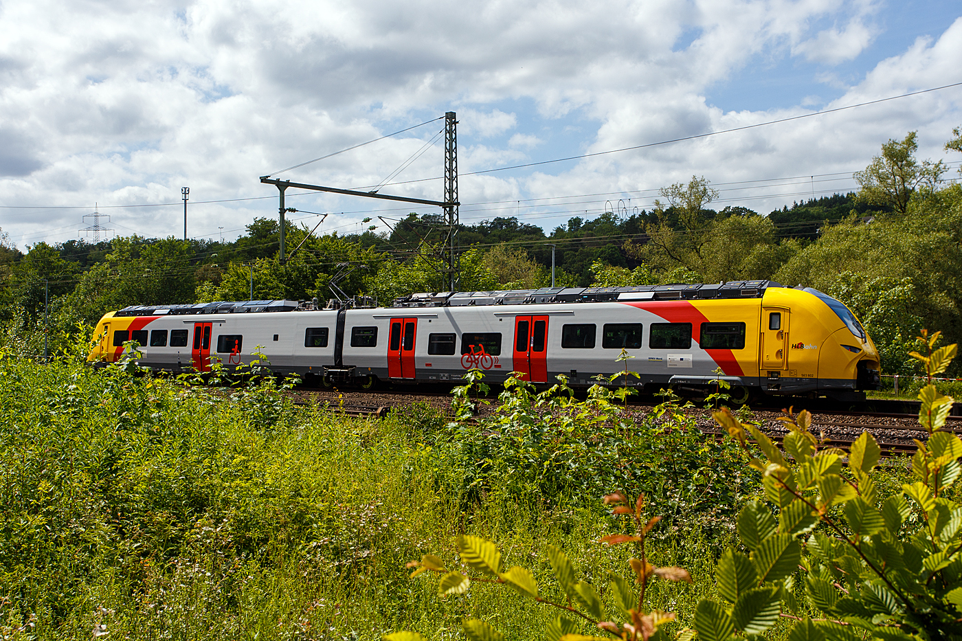 Der zweiteilige Hybridtriebzug SIEMENS Mireo Plus B, 563 802 / 563 902 (94 80 0563 802-8 D-HEB / 94 80 0563 902-6 D-HEB) der HLB (Hessische Landesbahn GmbH), als RB 90  Westerwald-Sieg-Bahn  (Siegen - Betzdorf/Sieg – Au/Sieg – Altenkirchen/Westerwald – Westerburg – Limburg/Lahn), erreicht am 07 Juni 2026 nun bald den Bahnhof Scheuerfeld/Sieg. 

Der zweiteilige SIEMENS Mireo Plus B wurden 2024/25 von SIEMENS in Krefeld gebaut und im April 2025 an die HLB ausgeliefert.

Als Ergebnis der von der HLB daf�r durchgef�hrten Fahrzeugausschreibung hatte Siemens Mobility den Zuschlag f�r drei zweiteilige Mireo Plus B Batteriez�ge erhalten. Das Fahrzeug mit seiner hohen Antriebsleistung ist f�r den anspruchsvollen Einsatz im Westerwald bestens geeignet. Der geplante Einsatz der drei Batteriez�ge auf den Linien RB 90 und RB 29 umfasst eine Jahresfahrleistung von fast 400.000 Zug-km und ersetzt drei Dieselfahrzeuge. Da die HLB emissionsfreien Bahnstrom bezieht, werden j�hrlich fast 1.150 Tonnen CO2 eingespart. Der Betrieb der Batteriefahrzeuge erfordert keine neue Infrastruktur, denn die Wendezeiten in Limburg von �ber 20 Minuten auf der RB 29 werden f�r die Aufladung der Fahrzeuge ausreichend sein. Bei den auf der RB 90 verkehrenden Batteriefahrzeugen erfolgt dies im elektrifizierten Abschnitt zwischen Au und Siegen. Die Oberwesterwaldbahn (Limburg – Au) ist mit der L�nge von rund 75 km und der zu �berwindende H�he von ca. 350 m derzeit in Deutschland die anspruchsvollste Strecke f�r den vorgesehenen Einsatz von Batteriez�gen. Aber auch auf der RB 96 „Hellertalbahn“ konnte man die schon oft sehen.

Technik und Fahrzeugaufbau:
Die Triebz�ge werden nur mit elektrischem Antrieb angeboten. Die Fahrzeugplattform ist mit Jakobs-Drehgestellen und Einzeldrehgestellen, �hnlich wie bei den ICE 4 mit innengelagerten Rads�tzen lieferbar. Die Wagenk�sten werden in Aluminium-Integralbauweise hergestellt. Bei diesem zweiteiligen Triebzug ruht je ein Wagenkasten auf einen Triebdrehgestell SF 7500 als Enddrehgestell, sowie auf der H�lfte des mittigen Jakobs-Laufdrehgestell SF 7500.

Die Triebz�ge werden im Siemens-Werk Krefeld gefertigt. Im M�rz 2020 erhielt Siemens Mobility den ersten Auftrag f�r eine zweiteilige Variante des Mireo Plus B die ihren Fahrstrom sowohl aus einer Batterie als auch aus der Fahrleitung erh�lt. Die Batterie kann im Stand und w�hrend der Fahrt aus der Fahrleitung geladen werden. Die Reichweite eines Mireo Plus B im Batteriebetrieb wird mit 80 bis 120 Kilometern angegeben.

Zum Einsatz kommen Lithiumtitanat-Akkumulatoren (LTO) von Toshiba, die unter den Wagenb�den verbaut sind. Diese haben eine hohe Zyklenfestigkeit auch bei hohen Ladestr�men, wie sie beim Bremsen und Anfahren auftreten – bei einer Laderate von 10C garantiert der Hersteller seit 2019 mindestens 15.000 Ladezyklen und seit 2022 mindestens 40.000 Ladezyklen.

TECHNISCHE DATEN:
Spurweite: 1.435 mm (Normalspur)
Achsfolge: Bo’2’Bo’
Fahrzeugl�nge �ber Kupplung: 46.560 mm
Drehzapfenanstand: 2 x 17.930 mm
Achsabstand im Triebdrehgestell (Enddrehgestell): 2.300 mm
Achsabstand im Jakobs-Laufdrehgestell: 2.600 mm
Drehgestellplattform: SF 7500 mit innengelagerten Rads�tzen
Raddurchmesser: 880 mm (neu) / 810 mm (abgenutzt)
Anzahl der T�ren je Seite: 3
Eigengewicht im betriebsbereiten Zustand: 92.891 kg
Installierte Leistung: 1.700 kW
Leistungs�bertragung: elektrisch
Motoren: 2 Drehstrom-Asynchronmotoren
H�chstgeschwindigkeit: 140 km/h
Kupplung: Mittelpufferkupplung Schaku Typ 10
Sitzpl�tze: 126
Bremse: FT C-el-pn-R-A-E-Mg (D)
kleinster befahrbarer Gleisbogen: R 150 m (Normal) / R 100 m (Werkstatt)
Zulassungen: Deutschland (D)