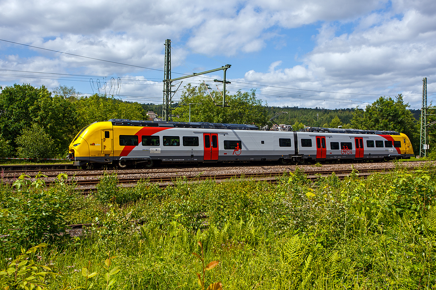 Der zweiteilige Hybridtriebzug SIEMENS Mireo Plus B, 563 802 / 563 902 (94 80 0563 802-8 D-HEB / 94 80 0563 902-6 D-HEB) der HLB (Hessische Landesbahn GmbH), als RB 90  Westerwald-Sieg-Bahn  (Siegen - Betzdorf/Sieg – Au/Sieg – Altenkirchen/Westerwald – Westerburg – Limburg/Lahn), erreicht am 07 Juni 2026 nun bald den Bahnhof Scheuerfeld/Sieg. 

Der zweiteilige SIEMENS Mireo Plus B wurden 2024/25 von SIEMENS in Krefeld gebaut und im April 2025 an die HLB ausgeliefert.

Als Ergebnis der von der HLB daf�r durchgef�hrten Fahrzeugausschreibung hatte Siemens Mobility den Zuschlag f�r drei zweiteilige Mireo Plus B Batteriez�ge erhalten. Das Fahrzeug mit seiner hohen Antriebsleistung ist f�r den anspruchsvollen Einsatz im Westerwald bestens geeignet. Der geplante Einsatz der drei Batteriez�ge auf den Linien RB 90 und RB 29 umfasst eine Jahresfahrleistung von fast 400.000 Zug-km und ersetzt drei Dieselfahrzeuge. Da die HLB emissionsfreien Bahnstrom bezieht, werden j�hrlich fast 1.150 Tonnen CO2 eingespart. Der Betrieb der Batteriefahrzeuge erfordert keine neue Infrastruktur, denn die Wendezeiten in Limburg von �ber 20 Minuten auf der RB 29 werden f�r die Aufladung der Fahrzeuge ausreichend sein. Bei den auf der RB 90 verkehrenden Batteriefahrzeugen erfolgt dies im elektrifizierten Abschnitt zwischen Au und Siegen. Die Oberwesterwaldbahn (Limburg – Au) ist mit der L�nge von rund 75 km und der zu �berwindende H�he von ca. 350 m derzeit in Deutschland die anspruchsvollste Strecke f�r den vorgesehenen Einsatz von Batteriez�gen. Aber auch auf der RB 96 „Hellertalbahn“ konnte man die schon oft sehen.

Technik und Fahrzeugaufbau:
Die Triebz�ge werden nur mit elektrischem Antrieb angeboten. Die Fahrzeugplattform ist mit Jakobs-Drehgestellen und Einzeldrehgestellen, �hnlich wie bei den ICE 4 mit innengelagerten Rads�tzen lieferbar. Die Wagenk�sten werden in Aluminium-Integralbauweise hergestellt. Bei diesem zweiteiligen Triebzug ruht je ein Wagenkasten auf einen Triebdrehgestell SF 7500 als Enddrehgestell, sowie auf der H�lfte des mittigen Jakobs-Laufdrehgestell SF 7500.

Die Triebz�ge werden im Siemens-Werk Krefeld gefertigt. Im M�rz 2020 erhielt Siemens Mobility den ersten Auftrag f�r eine zweiteilige Variante des Mireo Plus B die ihren Fahrstrom sowohl aus einer Batterie als auch aus der Fahrleitung erh�lt. Die Batterie kann im Stand und w�hrend der Fahrt aus der Fahrleitung geladen werden. Die Reichweite eines Mireo Plus B im Batteriebetrieb wird mit 80 bis 120 Kilometern angegeben.

Zum Einsatz kommen Lithiumtitanat-Akkumulatoren (LTO) von Toshiba, die unter den Wagenb�den verbaut sind. Diese haben eine hohe Zyklenfestigkeit auch bei hohen Ladestr�men, wie sie beim Bremsen und Anfahren auftreten – bei einer Laderate von 10C garantiert der Hersteller seit 2019 mindestens 15.000 Ladezyklen und seit 2022 mindestens 40.000 Ladezyklen.

TECHNISCHE DATEN:
Spurweite: 1.435 mm (Normalspur)
Achsfolge: Bo’2’Bo’
Fahrzeugl�nge �ber Kupplung: 46.560 mm
Drehzapfenanstand: 2 x 17.930 mm
Achsabstand im Triebdrehgestell (Enddrehgestell): 2.300 mm
Achsabstand im Jakobs-Laufdrehgestell: 2.600 mm
Drehgestellplattform: SF 7500 mit innengelagerten Rads�tzen
Raddurchmesser: 880 mm (neu) / 810 mm (abgenutzt)
Anzahl der T�ren je Seite: 3
Eigengewicht im betriebsbereiten Zustand: 92.891 kg
Installierte Leistung: 1.700 kW
Leistungs�bertragung: elektrisch
Motoren: 2 Drehstrom-Asynchronmotoren
H�chstgeschwindigkeit: 140 km/h
Kupplung: Mittelpufferkupplung Schaku Typ 10
Sitzpl�tze: 126
Bremse: FT C-el-pn-R-A-E-Mg (D)
kleinster befahrbarer Gleisbogen: R 150 m (Normal) / R 100 m (Werkstatt)
Zulassungen: Deutschland (D)