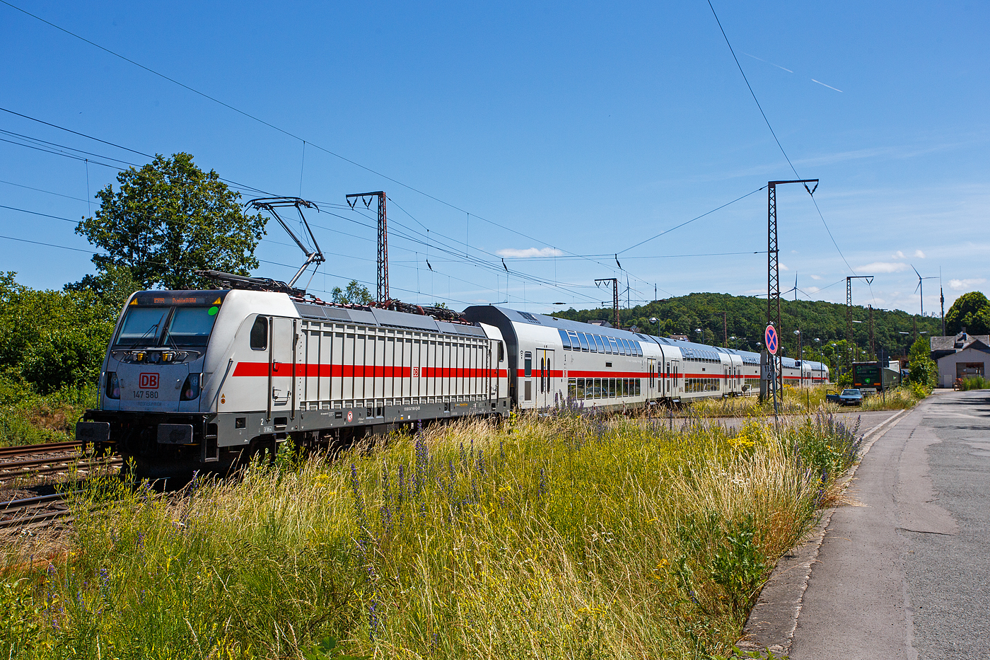 Die 147 580-5 (91 80 6147 580-5 D-DB - IC 4877) schiebt am 28 Juni 2024 die IC2-Garnitur 4877 der DB Fernverkehr AG Steuerwagen voraus, als IC 2229 / RE 34 - Umlauf RE 52229 (Dortmund Hbf – Siegen – Dillenburg - Frankfurt/Main Hbf), durch Wilnsdorf-Rudersdorf (Kreis Siegen) in Richtung Frankfurt/Main. Zwischen Dortmund Hbf und Dillenburg wird der Zug auch als RE 34 (hier Umlauf 52229) geführt und hat in diesem Abschnitt die Freigabe für alle Nahverkehr Tickets.

Die TRAXX P160 AC3 wurde 2020 von Bombardier in Kassel unter der Fabriknummer 35663 gebaut und an die DB Fernverkehr AG ausgeliefert. Sie hat die Zulassungen für Deutschland und die Schweiz, daher hat sie auch vier Stromabnehmer. Der Bahnstrom (15.000 V 16 ⅔ Hz) ist ja derselbe, aber die Palettenbreite (Wippe) ist 1.450 mm im SBB-Netz und somit 500 mm schmaler als die Wippen fürs DB Netz (1.900 mm breit). Das Schleifleistenmaterial ist bei beiden aus Graphit.