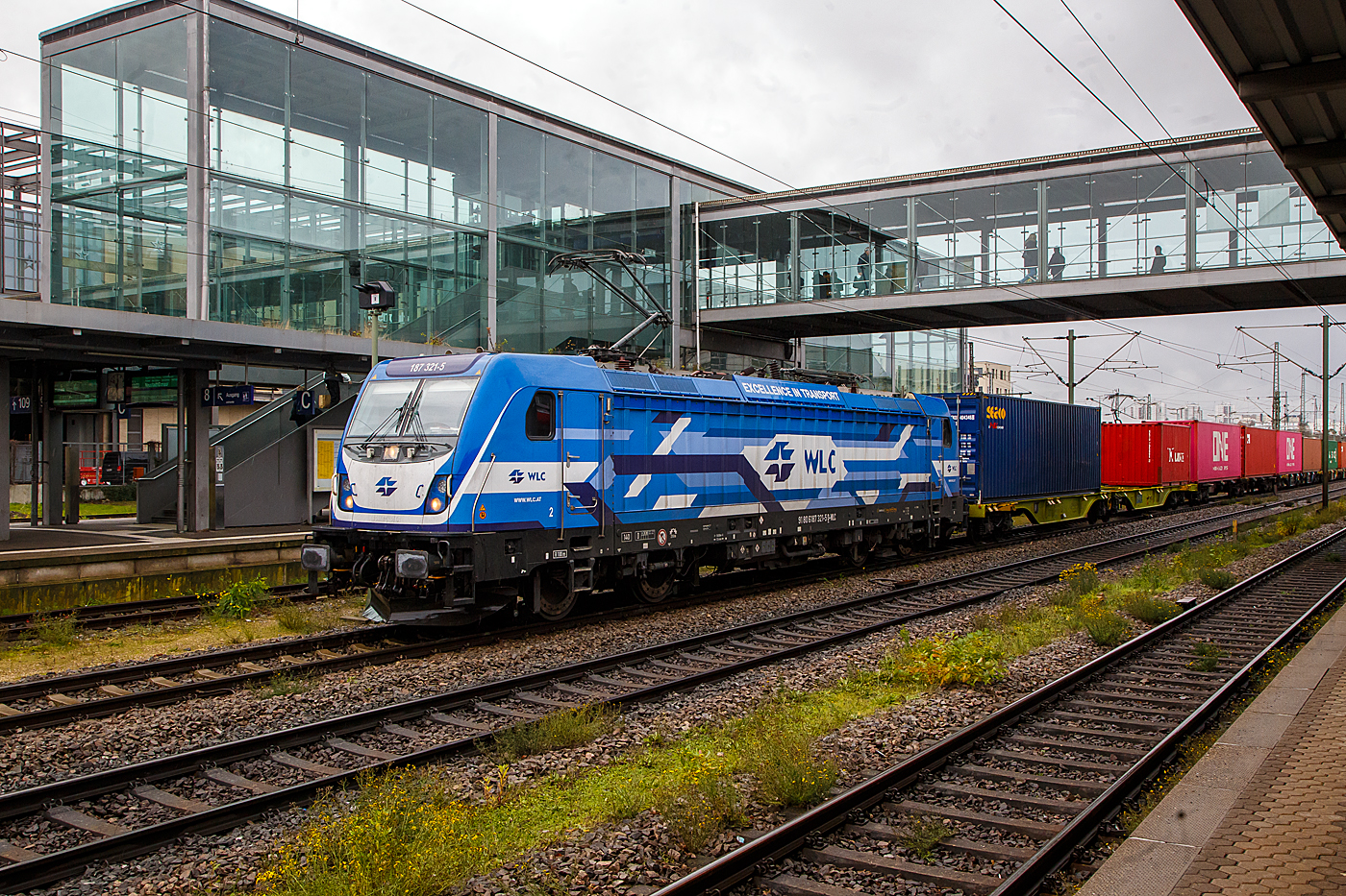 Die 187 321-5 (91 80 6187 321-5 D-WLC) der WLC - Wiener Lokalbahnen Cargo GmbH (Wien) fährt am 24.11.2022 mit einem Containerzug durch den Hauptbahnhof Regensburg.

Die Lok Bombardier TRAXX F140 AC3 LM (zugelassen für 140 km/h daher Variante F140 und nicht F 160). Sie wurde 2017 von Bombardier in Kassel unter der Fabriknummer 35229 gebaut und an die WLC - Wiener Lokalbahnen Cargo GmbH (Wien). Nach meiner Sichtung hat die Lok die Zulassung für Deutschland (D) und Österreich (A). Für Ungarn und Rumänien sind die Zulassungen noch nicht erteilt (H und RO sind durchgestrichen).

Wie die Vorgängerinnen AC1 und AC2 ist die AC3 für den Betrieb unter 15 Kilovolt bei 16,7 Hertz, sowie unter 25 Kilovolt bei 50 Hertz Wechselstrom ausgelegt, und verfügt unverändert über eine Dauerleistung von 5.600 kW ( Power Boost  von 6.000 kW) und eine Anfahrzugkraft von 300 kN. Von den Traxx 2E übernommen wurde der Maschinenraum mit Seitengang um das sogenannte Powerpack, bestehend aus Stromrichter und Hochspannungsgerüst, womit erstmals alle Varianten dasselbe Layout verwenden.

Neu ist die Kopfform der Traxx-3-Lokomotiven, im Wesentlichen ein auf dem Lokkasten aufgesetztes GFK-Modul. Zudem wurden die Lokomotiven erstmals ab Werk konstruktiv für den Einbau der Zugbeeinflussung ETCS vorbereitet. Neuerungen betreffen die verfügbaren Drehgestelle: zu den bisherigen Varianten „F140“ mit Tatzlagerantrieb und Zulassung für maximal 140 km/h, und „P160“ mit Hohlwellenantrieb und Zulassung für maximal 160 km/h, werden die Traxx-3-Lokomotiven offiziell auch als Variante „F160“ mit Tatzlagerantrieb und Zulassung für maximal 160 km/h angeboten. Es gibt sie also als TRAXX F140 AC3 und als TRAXX F160 AC3.

Gänzlich neu sind die optional verfügbaren Last-Mile-Module, die es als Last-Mile-Diesel (LMD) mit zusätzlicher Last-Mile-Battery (LMB) gibt. Das LMD besteht aus einem Dieselhilfsmotor und einem Kraftstofftank, um auch nicht-elektrifizierte Streckenabschnitte und Anschlussgleise befahren zu können. Der Dieselmotor von Deutz verfügt über einen Hubraum von 7.150 cm³, erbringt eine Leistung von 230 kW (180 kW am Rad), mit Batterieunterstützung 290 kW und erfüllt die Stage-IIIB-Abgasnorm. Im Dieselbetrieb werden alle vier Fahrmotoren betrieben, die Anfahrzugkraft beträgt dabei mit Batterieunterstützung unverändert 300 kN, ohne Batterie 260 kN. Ohne Anhängelast ist damit eine Höchstgeschwindigkeit von 60 km/h möglich, bei 2000 Tonnen Last noch 40 km/h. Der Tankinhalt von 400 Litern reicht für bis zu acht Stunden Dieselbetrieb, kurze Strecken können auch ausschließlich mit der eingebauten Batterie zurückgelegt werden. Der Übergang vom elektrischen zum Dieselbetrieb kann während der Fahrt erfolgen. Für den Rangierbetrieb ist zudem eine Funkfernsteuerung erhältlich.

Erstmals wurde der Lokkasten nicht mit glatten Seitenwänden gefertigt, sondern konstruktiv deutlich günstiger, sind die Seitenwände der AC3 vertikal gesickt und die Seitenflächen erhielten sogenannte Flex-Panels, eine Vorrichtung zum Einspannen von Planen. Diese würden die Sicken verdecken, und wären kostengünstiger als Umlackierungen oder Umbeklebungen. Die Nutzung der Flex-Panels wurde jedoch in der Schweiz umgehend untersagt.

TECHNISHE DATEN:
Hersteller: 	Bombardier Transportation
Spurweite: 	1.435 mm (Normalspur)
Achsanordnung: Bo’ Bo’
Länge über Puffer: 18.900 mm
Drehzapfenabstand: 10.440 mm
Achsabstand im Drehgestell: 2.600 mm
Treibraddurchmesser: 	1.250 mm (neu) / 1.170 mm (abgenutzt)
Höhe:  4.283 mm
Breite:  2.977 mm
Lichtraumprofil: UIC 505-1
Dienstgewicht: 87 t
Fahrmotoren: 4 Asynchronmotoren
Bremse: Elektrische Bremse (SW-GPR-E mZ)

Daten im Oberleitungsbetrieb:
Höchstgeschwindigkeit: 160 km/h
Dauerleistung: 5.600 kW 
Kurzzeitleistung  Power Boost : 6.000 kW
Anfahrzugkraft: 300 kN
Dauerzugkraft: 252 kN bei 80 km/h
Stromsystem: 15 kV 16,7 Hz~ und 25 kV 50 Hz~

Daten im Dieselbetrieb (Last-Mile):
Nenndrehzahl: 1.800 U/min
Höchstgeschwindigkeit: 60 km/h
Dauerleistung: 320 kW (Quelle WLC)
Tankinhalt:  400 l
