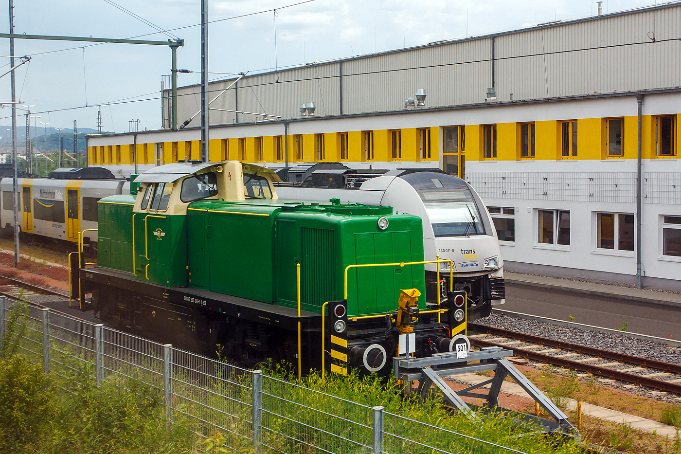 Die 295 049-1 (98 80 3295 049-1 D-BEG) der BE - Brohltal-Schmalspureisenbahn Betriebs-GmbH, ex DB 295 049-1, ex DB 291 049-5, ist am 17 Juni 2013 beim Betriebswerk der trans regio Deutsche Regionalbahn GmbH in Koblenz-Moselweiß abgestellt. Das Bild konnte ich einem Zug heraus machen. 

Die V 90 wurde 1976 von Arnold Jung Lokomotivfabrik GmbH in Jungenthal, Kirchen a.d. Sieg unter der Fabriknummer 14213 gebaut und als 291 049-5 an die Deutsche Bundesbahn geliefert. Die V90 war die vorletzte von Jung in Kirchen gebaute Lokmotive überhaupt. Im Jahr 2003 erfolgte der Umbau auf Funkfernsteuerung und die Umzeichnung in DB 295 049-1. Bei der DB Schenker Rail Deutschland AG war sie bis 2013 im Bestand, wurde aber am 04.11.2011 z-gestellt und am 07.03.2013 ausgemustert. Im März 2013 ging sie dann an die Brohltal-Schmalspureisenbahn Betriebs-GmbH.

Die Entwicklung der BR 291/295:
Im Jahre 1965 baute die MaK auf eigene Rechnung eine Serie von fünf Loks, die auf der V 90 basierten, jedoch statt des 12-Zylinder-V-Motors (MTU MB 12 V 652 TA 10) der V 90 einen hauseigenen 8-Zylinder-Reihenmotor mit Abgasturbolader vom Typ 8M 282 AKB erhielten. Dessen Leistung betrug abhängig von der eingestellten Drehzahl zwischen 1100 PS bei 930/min und 1400 PS bei 1100/min. Die Loks erhielten die Bezeichnung V 90 P. Der Hersteller erhoffte sich Aufträge von Privatbahnen und der Industrie, daher das „P“.

Die DB übernahm im August 1965 die V 90 P 03 und im letzten Quartal 1966 die beiden V 90 P 04 und V 90 P 05 als Mietloks zu Testzwecken. Deren Leistungen am Ablaufberg entsprachen so sehr den Anforderungen, dass eine Bestellung über hundert Maschinen erfolgte. Die DB erwarb die drei V 90 P im Juli 1972, nachdem sie sie bei der Umstellung auf Computernummern schon als Unterbaureihe 2919 eingereiht hatte.

Da sich die V 90 P aufgrund ihrer bundesbahntypischen Bordelektrik (110 V statt der bei NE-Bahnen üblichen 24 V), sowie ihrer konsequenten Auslegung für den schweren Rangierdienst nicht bei den Privatbahnen durchsetzen konnte, entwickelte MaK die V 90 P weiter zur MaK G 1600 BB, von welcher 16 Stück gebaut wurden.

Die Serienloks der BR 291 wurden von 1974 bis 1978 an die Deutsche Bundesbahn ausgeliefert. Bei der MaK in Kiel wurden davon die 291 001 bis 040, sowie die 291 051 bis 100 gebaut. Die Maschinen 291 041 bis 050 kamen dagegen aus Kirchen a.d. Sieg von Jung, die zugleich die letzten von dieser Fabrik gebauten Loks waren.

TECHNISCHE DATEN:
Spurweite: 1.435 mm
Achsanordnung: B'B'
Länge über Puffer: 14.320 mm
Breite: 3.100 mm
Drehzapfenabstand: 7.000 mm
Gesamtachsstand: 9.500 mm
Höchstgeschwindigkeit: 80 km/h Streckengang / 40 km/h Rangiergang
Dienstgewicht: 80 t
Anfahrzugkraft im Schnellgang:188 kN
Anfahrzugkraft im Langsamgang: 236 kN

Motorbauart: MaK 8-Zylinder- Viertakt-Diesel- Reihenmotor mit Abgasturbolader
Motortyp: 8M 282 AKB
Leistung: 1030 kW / 1400
Dauerleistung: 800 kW (1100 PS)
Nenndrehzahl: 950 U/min
Hubraum: 101 l (Bohrung Ø 240 mm x 280mm Hub)
Motorengewicht: 8.990kg

Getriebe und Leistungsübertragung:
Das hydraulische Getriebe von Voith hat zwei Wandlergänge. Ein mechanisches Nachschaltgetriebe ermöglicht die Wahl zwischen einem Schnell- und einem Langsamgang sowie den Wechsel der Fahrtrichtung. Um feinfühlige Langsamfahrten zu ermöglichen, hat das Getriebe eine stufenlos regelbare Wandlerteilfüllung. Die Leistungsübertragung auf die Achsgetriebe erfolgt dann über Gelenkwellen
