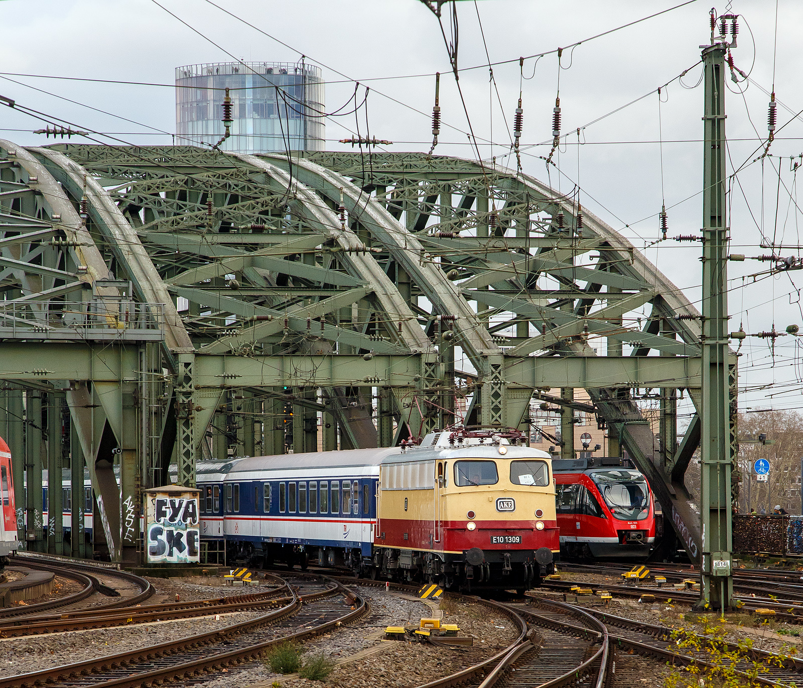 Die AKE E10 1309 (91 80 6113 309-9 D-TRAIN) der Train Rental International GmbH mit n-Wagen als National Express Verstrker des RE 1  Nordrhein-Westfalen-Express  Dortmund Hbf – Kln Hbf, verlsst am 22.12.2018 gerade die Hohenzollernbrcke und fhrt bald in den Hbf Kln ein.
