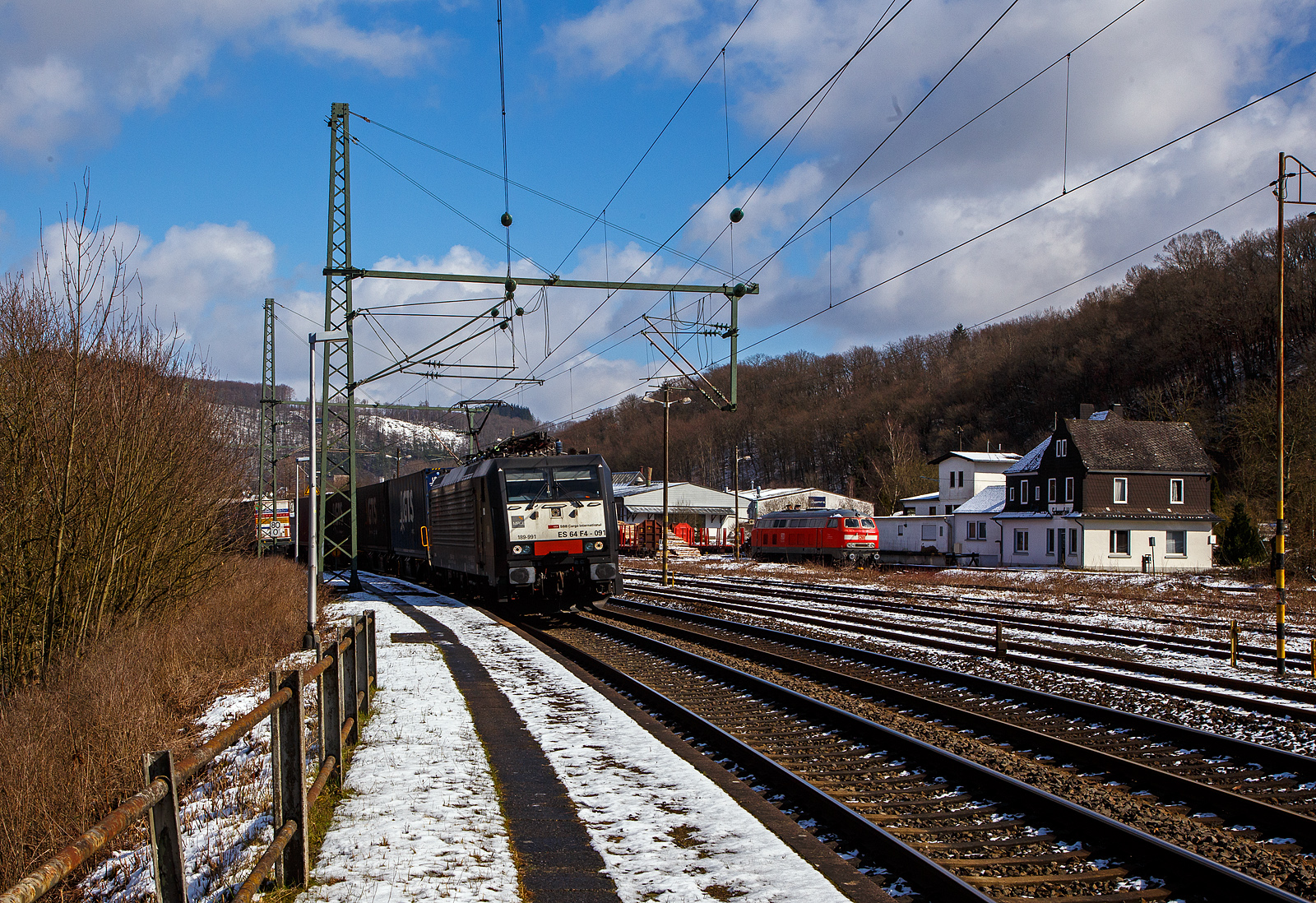 Die an die SBB Cargo International AG vermietete MRCE Dispolok ES 64 F4 - 091 bzw. 189-991 / LZB 189 991-3 (91 80 6189 991-3 D-DISPO, Class 189-VE) fährt am 15.03.2023, mit einem KLV-Zug auf der Siegstrecke (KBS 460) durch Scheuerfeld (Sieg) in Richtung Köln. Während hinten beim Kleinbahnhof der WEBA (Westerwaldbahn) die 218 191-5 (92 80 1218 191-5 D-MZE) der MZE - Manuel Zimmermann Eisenbahndienstleistungen abgestellt ist.

Die SIEMENS EuroSprinter wurde 2004 von SIEMENS in München-Allach unter der Fabriknummer 20739 gebaut.

Die BR 189 (Siemens ES64F4) hat eine Vier-Stromsystem-Ausstattung. Sie ist in allen vier in Europa üblichen Bahnstromsystemen einsetzbar. Diese hier hat die Variante E und besitzt die Zugbeeinflussungssysteme LZB/PZB, ETCS, SCMT, ZUB, INTEGRA und ATB für den Einsatz in Deutschland, Österreich, Schweiz, Italien, Niederlande, Slowenien und Rumänien.

Die Stromabnehmerbestückung ist folgende:
Pos. 1: CH, FR (AC), LU (AC), BE (AC)
Pos. 2: IT, SI, HR (DC)
Pos. 3: NL (DC), CZ (DC), FR (DC), SK, LU (DC)
Pos. 4: DE, AT, NL (AC), DK, CZ (AC), HR (AC), HU, RO