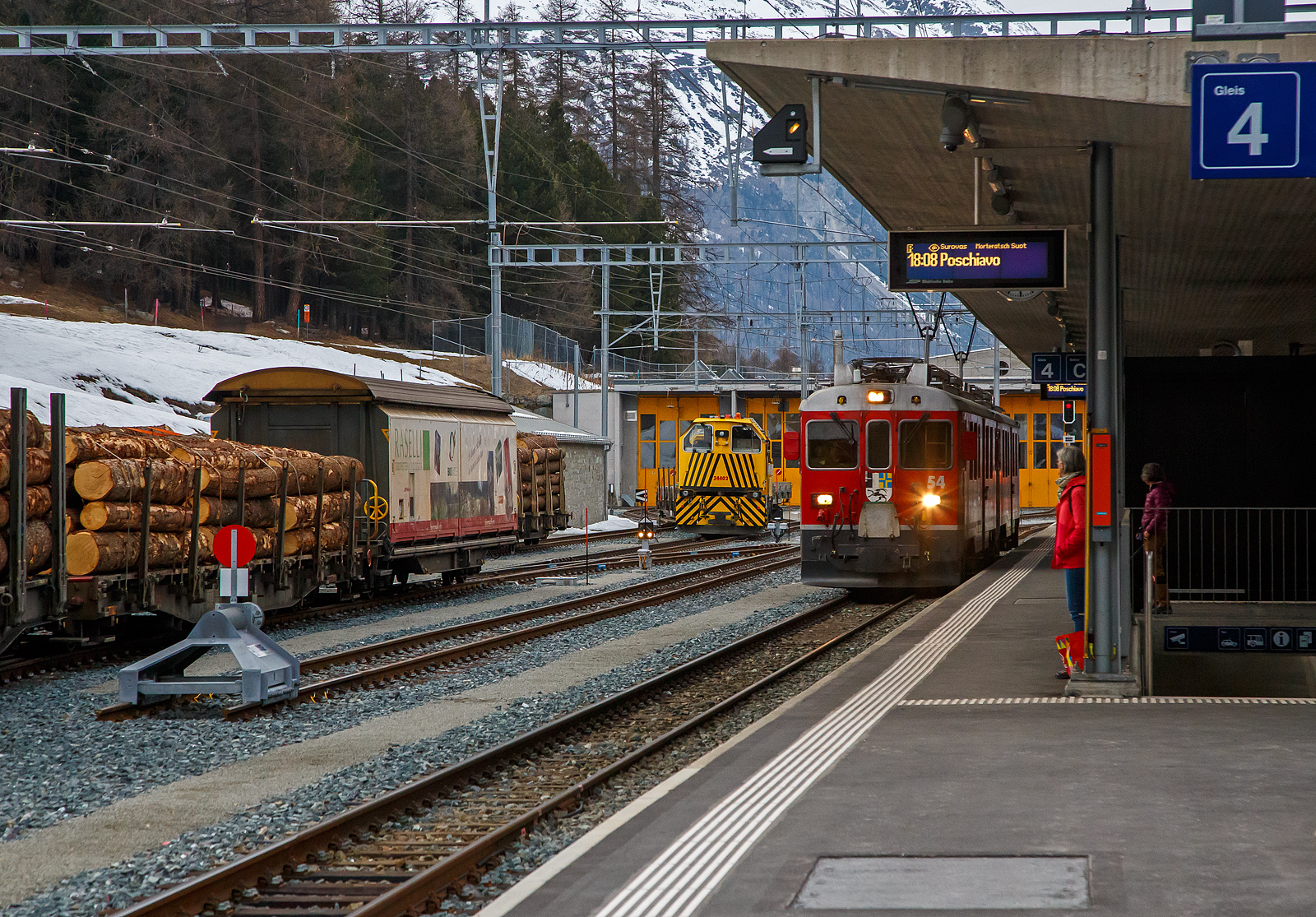 Die beiden RhB ABe 4/4 III Triebwagen 54  Hakone  und  51  Poschiavo  erreichen am 21.03.2023, als RhB-Regionalzug von St. Moritz nach Poschiavo, den Bahnhof Pontresina. Noch ist es ein reiner Personenzug, hier im Bahnhof wird er zum PmG (Personenzug mit Güterbeförderung), denn er bekommt hier 3 mit Holz beladene vierachsige Flachwagen vom Typ “Sp-w“ angehangen. Bei der Fahrt hinauf nach Ospizio Bernina merkten wir wie die Triebwagen arbeiten mussten. 

Als ABe 4/4 III werden bei der Rhätischen Bahn (RhB) die 1988 und 1990 beschafften Gleichstrom-Elektrotriebwagen mit den Betriebsnummern 51 bis 56 bezeichnet. Die Schlepptriebwagen werden nur auf der Berninabahn eingesetzt, wo sie die Verkehrszunahme bewältigen helfen. 

Die von SWA (Schindler Waggon AG in Altenrhein) und BBC (Brown, Boveri & Cie. in Baden) in zwei Serien (1988 und 1990)zu je drei Stück gebauten und gelieferten Triebwagen waren seinerzeit die ersten RhB-Triebfahrzeuge in Umrichtertechnik mit Drehstrom-Asynchronmotoren. Zudem gehörten sie weltweit zu den ersten Gleichstromtriebfahrzeugen mit GTO-Thyristoren. Sie sind 65 km/h schnell, 47 Tonnen schwer und waren mit einer Stundenleistung von 1.016 kW bei Ablieferung die stärksten Gleichstromtriebwagen der RhB. Ihre Anhängelast bei 70 Promille Steigung beträgt 90 beziehungsweise 95 Tonnen, sofern nur Vierachser im Zug sind. Sie weisen zwölf Sitzplätze in der ersten und 16 in der zweiten Klasse auf. Dank Vielfachsteuerung können sie untereinander und auch mit den älteren ABe 4/4 II 41–49 sowie Gem 4/4 801–802 in Doppeltraktion fahren, wovon im täglichen Betrieb reger Gebrauch gemacht wird. Eine Doppeltraktion von zwei ABe 4/4 III hat theoretisch eine Leistungsreserve für die Beförderung von weiteren 50 Tonnen, da die maximale Zughakenlast von 140 Tonnen auf der Berninabahn nicht überschritten werden darf.

TECHNISCHE DATEN:
Gebaute Anzahl: 6 (Nummerierung 51 – 56)
Hersteller: SWA / BBC
Baujahre: 1988 und 1990
Achsformel: Bo′Bo′
Spurweite: 1.000 mm
Länge über Puffer: 16.886 mm
Radstand : 13.010 mm
Breite: 2.650 mm
Dienstgewicht: 47 t 
Höchstgeschwindigkeit: 65 km/h
Dauerleistung: 1.016  kW
Anfahrzugkraft: 178 kN
Stundenzugkraft: 108 kN bei 34 km/h
Stromsystem: 1 kV DC (Gleichstrom)
Stromübertragung: 2 Einholmstromabnehmer
Steuerung:  GTO-Thyristor
Sitzplätze: 1. Klasse: 12 / 2. Klasse: 16
