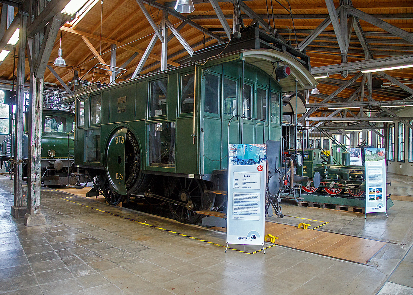 Die Drehstrom- Elektrolokomotive ex BTB De 2/2 Nr.1, ex BTB F 2/2 Nr. 1 (1902 – 1922), ex BTB E2E Nr. 1 (bis 1902), am 11.09.2022 in der Lokwelt Freilassing. Die Lok ist Eigentum des Deutschen Museums - Verkehrszentrum in Mnchen und eine Leihgabe die Lokwelt Freilassing

Dem Gterverkehr der Burgdorf-Thun-Bahn (BTB) dienten zwei Lokomotiven vom Typ F 2/2. Bis 1902 wurden sie als E2E bezeichnet, ab 1922 als De 2/2. Diese beiden ersten in der Schweiz, im Jahr 1899, gebauten elektrischen Lokomotiven (De 2/2 Nr.1 und  2) waren eine gemeinsame Konstruktion der Schweizerischen Lokomotiv- und Maschinenfabrik (SLM) in Winterthur fr den mechanischen Teil und der Brown, Boveri & Cie. (BBC) fr die elektrische Ausrstung. 

Der noch nicht ausgereifte Einphasen-Wechselstrom-Betrieb konnte zur damaligen Zeit noch nicht eingesetzt werden. Deshalb beschaffte die Schweizer Burgdorf-Thun-Bahn (BTB) zunchst fr den reinen Gterzugbetrieb zwei dieser mit Drehstrom (Dreiphasenwechselstrom) angetriebenen Lokomotiven. Das Drehstrom-System konnte nur in einem bestimmten Geschwindigkeitsbereich effektiv arbeiten, so dass ein mechanisches Schaltgetriebe fr zwei maximale Geschwindigkeiten notwendig war, nmlich fr 18 und 36 km/h.

Ab 1933 wurde der Drehstrombetrieb auf dieser Strecke eingestellt und die beiden Lokomotiven ausgemustert. Die beiden Lokomotiven sind als weltweit erste Drehstromlokomotiven fr den Vollbahnbetrieb erhalten geblieben. Die Nr. 1 befindet in der Lokwelt Freilassing, die Nr. 2 befindet sich im Verkehrshaus der Schweiz in Luzern.

Die beiden Motoren wiesen eine Leistung von je 150 PS (110 kW) auf. Das nur im Stillstand umschaltbare Getriebe ermglichte zwei Geschwindigkeiten, Die eine bis 18 km/h lie auf der grten Steigung von 25 ‰ eine Anhngelast von 100 Tonnen zu, die andere bis 36 km/h noch die Hlfte. Wobei die zulssige Hchstgeschwindigkeit betrug 50 km/h, so wurde in den spteren Betriebsjahren in Gefllen stromlos gefahren, um diese zu erreichen. Dank der hheren Geschwindigkeit htten die Lokomotiven ntigenfalls auch im Personenverkehr Verwendung finden knnen.

Die beiden 19-poligen Triebmotoren sind beidseits auf einer auf einem Hilfsgestell gelagerten gemeinsamen Welle montiert. ber ein Vorgelege wurde das Drehmoment mittels Kuppelstangen auf die beiden Achsen bertragen. Zum Anfahren war ein fr beide Motoren gemeinsamer Widerstand vorhanden, der mit dem in jedem Fhrerstand vorhandenen Kontroller allmhlich ausgeschaltet wurde. Beleuchtung, Heizung und Hilfsbetriebe wurden mit einer Spannung von 100 Volt betrieben. Die Lokomotiven weisen an beiden Enden offene Plattformen auf. Die vier Schleifbgel auf dem Dach legten sich selbstttig beim Wechsel der Fahrtrichtung nach hinten um. Zum Abbgeln mussten die an den Bgeln angebrachten kurzen Zugseile vom Boden aus mit hlzernen Stangen heruntergezogen und in Arretierhaken eingehngt werden.

TECHNISCHE DATEN:
Baujahr: 1899, Ausmusterung1930
Spurweite: 1.435 mm (Normalspur)
Achsfolge: B
Lnge ber Puffer: 7.800  mm
Achsabstand: 3.140 mm
Treibraddurchmesser:  1.230 mm
Dienstgewicht: 29.600 kg
Hchstgeschwindigkeit: 18 km/h / 36 km/h (stromlos bergab 50 km/h)
Stundenleistung: 300 PS (220 kW)
Stundenzugkraft: 4.400 daN
Stromsystem: 750 V, 40 Hz ∆
Anzahl der Fahrmotoren: 2
bersetzungsstufen: 2 (fr 18 / 36 km/h)

Die Burgdorf-Thun-Bahn (BTB) war eine Eisenbahngesellschaft in der Schweiz. Ihre Strecke von Burgdorf ber Konolfingen nach Thun wurde als erste elektrische Vollbahn der Schweiz im Jahr 1899 dem Betrieb bergeben. Heute ist sie Bestandteil der BLS AG