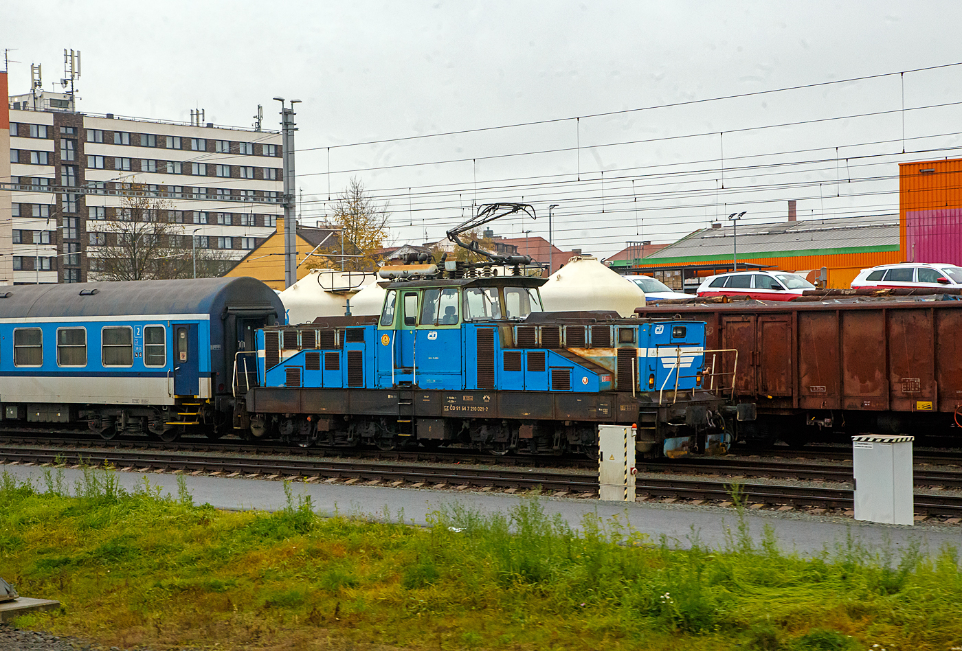 Die elektrische AC-Rangierlokomotive ČD 210 021-2 (CZ ČD 91 54 7 210 021-2) der České dráhy (ČD) steht am 24.11.2022 bei Pilsen (Plzeň) mit einem Personenzug (aufgenommen aus einem alex-Zug).

Die ČD Baureihe 210, ex ČSD-Baureihe S 458.0 (ab 1988 Baureihe 210) ist eine elektrische Rangierlokomotive für 25 kV 50 Hz Wechselstrom.  Sie wurde gleichzeitig mit der Gleichstromlok E 458.0 (heute BR 110) entwickelt, um auf größeren Personen- sowie Güterbahnhöfen den Verschub sowie die Beförderung von Übergabefahrten durchzuführen. Der mechanische Teil ist identisch mit dem der E 458.0, nur im elektrischen Aufbau hat die Lokomotive einen Trafo und eine andere Steuerung. Eine minimale Geschwindigkeit bis zu 5 km/h ist möglich. Die Lokomotiven sind mit einem speziellen Trafo für die Beheizung des Zuges mit 1,5 kV bzw. 3 kV 50 Hz ausgerüstet, und können somit auch im Personenzugdienst eingesetzt werden. Das Übersetzungsverhältnis zwischen Fahrmotorritzel und Großrad beträgt 1:4,055, was der Lokomotive eine Höchstgeschwindigkeit von 80 km/h ermöglicht. Für den Betrieb auf nicht elektrifizierten Streckenteilen besitzt die Lok Akkumulatoren.

TECHNISCHE DATEN:
Gebaute Stück: 74
Spurweite: 1.435 mm (Normalspur)
Achsformel: Bo’Bo’
Länge über Puffer: 14.400 mm
Rahmenlänge:  13.160 mm
Breite: 3.000 mm
Höhe (Pantograph gesenkt):  4.625 mm
Achsstand im Drehgestell : 2.800 mm
Drehzapfenabstand:  6. 300 mm
Treibradraddurchmesser: 1.050 mm (neu) / 980 mm (abgenutzt)
Kleister befahrb. Kurvenradius: R 120 m
Dienstgewicht: 72 t
Max. Achslast : 18 t
Stundenleistung: 984 kW
Dauerleistung: 880 kW
Anfahrzugkraft:  max. 164 kN
Fahrmotoren: 4 Stück Typ TE 006 
Stromsystem: 25 kV 50 Hz AC (Wechselstrom)