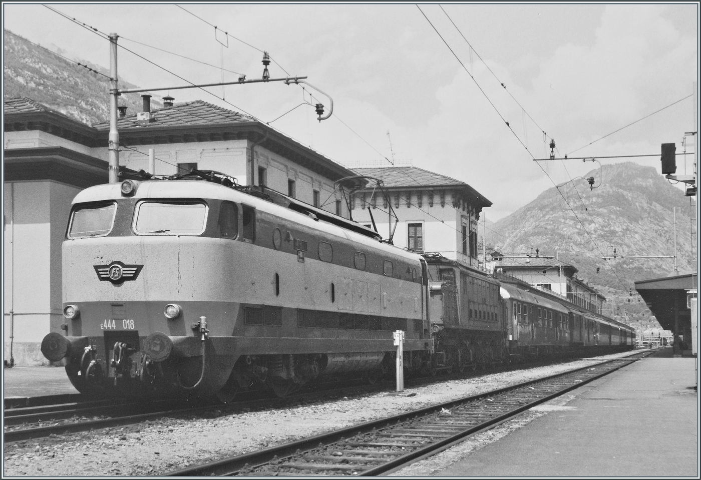 Die formsch�ne FS E 444 018  Tartaruga  (Schildkr�te) in einem eher ungewohnten Aufgabenbereich: Die Schnellzuglok �bernimmt in Domodossola  einen Regionalzug inklusive der  kalten  E 626 in Richtung Milano. 
Die FS verf�gte �ber 117 Loks dieser Baureihe, die mit einer maximalen Geschwindigkeit von 180 km/h im schnellen Schnellzugsverkehr zum Einsatz kamen, sp�ter aber im Frontbereich optisch wenig vorteilhaft umgebaut wurden aber noch lange Zeit im Einsatz standen.

Analogbild vom Mai 1985 