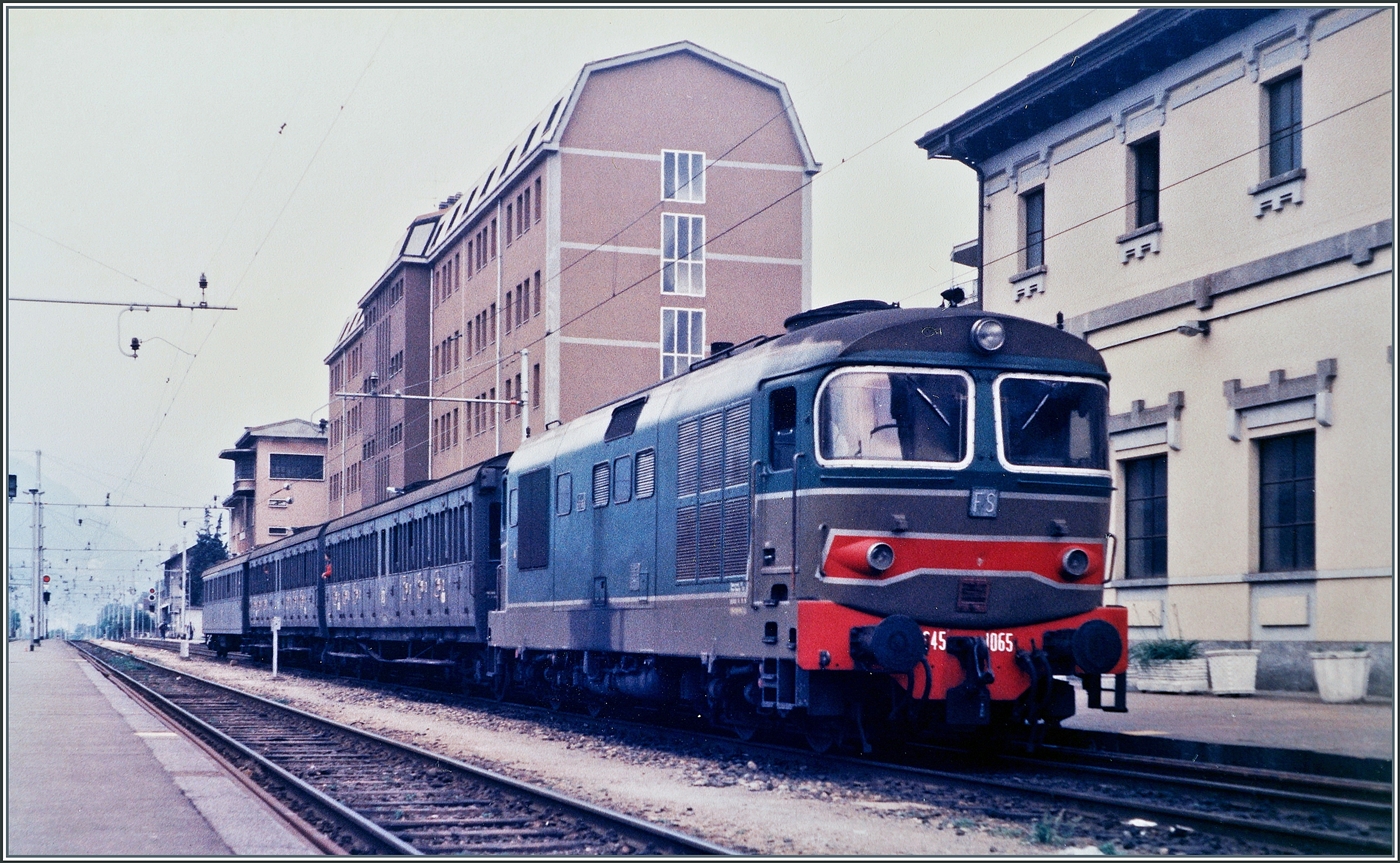Die FS D 345 1065 erreicht mit ihrem Regionalzug von Novara ihre Ziel Domodossola. Die ersten zwei Wagen tragen die Sammelbezeichnung  Centoporte ,  was auf Deutsch  Hundertt�renwagen  bedeutet. Von 1930 bis Mitte der 1980 waren etwa 2000 Wagen in verschiedene Ausf�hrungen im Einsatz. Da dieses Bild 1985 entstand, waren d�rfte es sich bereits im eine der letzten Eins�tze dieser Wagen gehandelt haben. 

Analogbild vom Mai 1985