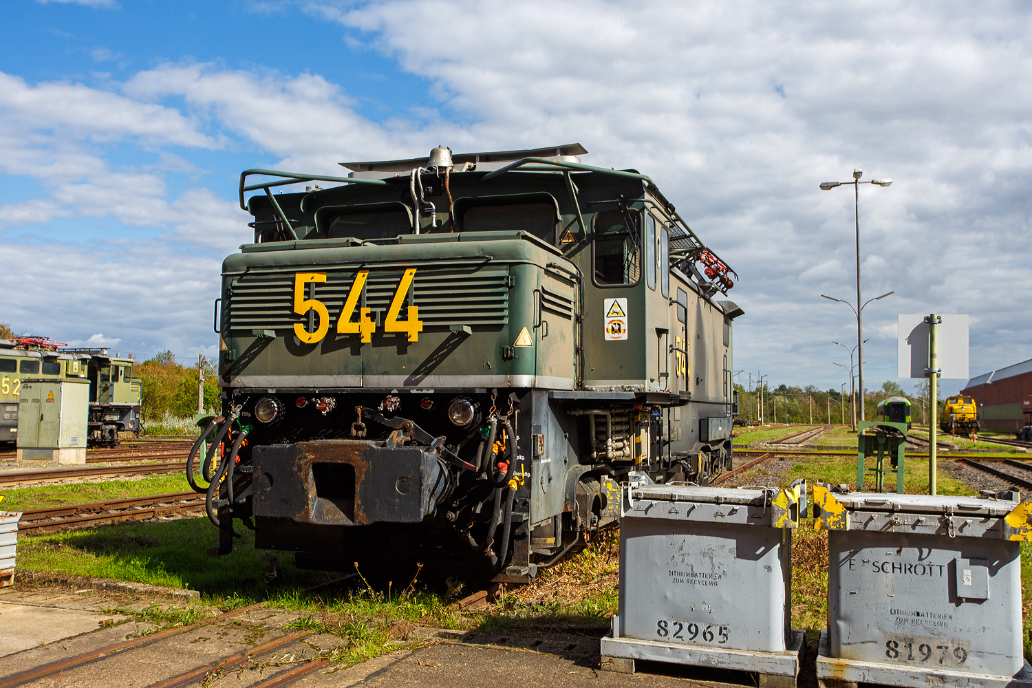 Die m�chtige Tagebaulokomotive El 1 – 544 der RWE Power AG (ex Rheinbraun) steht am 18 September 2026 in der Hauptwerkstatt Grefrath der RWE Power AG (Kompetenzzentrum f�r Schienenfahrzeuge in Frechen-Grefrath).

Das Foto entstand:
Im Rahmen von dem „Tag der Schiene“ wurden am Freitag den 18 September 2026 hier Werkstattf�hrungen angeboten. Die Teilnehmerzahl war pro Gruppe auf 15 Personen begrenzt. So kamen wir in den Genuss spannende Einblicke in das Tagesgesch�ft der modernen Instandhaltungstechnik und die vielf�ltigen Aufgaben der RWE Mitarbeiter zu bekommen. Im Zuge des Strukturwandels, wegen dem Kohleausstieg, �ffnet die RWE-Hauptwerkstatt Grefrath seine Tore f�r den externen Markt. Umfangreich modernisiert und ECM-Zertifiziert nach DVO EU 2019/779, f�r die Instandhaltung von G�terwagen, Lokomotiven, Triebz�gen sowie Bau-/Instandhaltungsfahrzeug. Heute werden schon einige externe Fahrzeuge dort instandgehalten, f�r diese galt es aber ein „Fotoverbot“ zu respektieren. 
Damit auf der Schiene alles l�uft…
…wird die Instandhaltung Bahn im Zuge des Strukturwandels zu einem wichtigen Zukunftsbereich der RWE Power AG

Die Tagebaulokomotive
Die elektrischen Tagebaulokomotiven EL 1 wurden von einem Konsortium, bestehend aus den Firmen Henschel, Krupp, Krauss-Maffei, Siemens-Schuckertwerke, AEG und Brown, Boveri & Cie., in der Zeit von 1954 bis 1965 in 117 Exemplaren f�r die Rheinischen Braunkohlenwerke (sp�ter Rheinbraun, heute RWE Power AG) gefertigt. Die Lok 544 wurde 1956 von Krauss-Maffei in M�nchen-Allach unter der Fabriknummer 18204 gebaut, der elektrische Teil ist von AEG. Sie ist aktuell noch eine von 21 El 1 Loks im Einsatzbestand.

Geschichte
Da sich im Braunkohlebergbau im Tagebaubetrieb das Verh�ltnis Kohle/Abraum st�ndig verschlechterte, waren die Abbaubetriebe zu neuen L�sungen bei der F�rdertechnik gezwungen, um am Markt konkurrenzf�hig zu bleiben.

Bei Rheinbraun vergr��erten sich dazu die F�rderwege durch stillgelegte Tagebaue. Das Unternehmen entschloss sich daher, die neue Nords�dbahn zum Tagebau Garzweiler in Normalspur anzulegen, was den Bau einer v�llig neuen Lokomotive bedingte. Diese Maschine sollte bei den Fahrmotoren die bew�hrte Gleichstromtechnik behalten, f�r die Fahrleitung wurde Wechselspannung mit der Industriefrequenz 50 Hz verwendet.

1955 wurden die ersten Lokomotiven geliefert. Ihre Aufgabe war die Bef�rderung eines Zuges mit acht Kohlewagen von 100 m� Fassungsverm�gen mit einem Gesamtgewicht von ungef�hr 2000 t. Auf den Strossengleisen sollten sie im Kriechgang eine Geschwindigkeit von 1 km/h nicht �berschreiten, und als H�chstgeschwindigkeit sollten 70 km/h erreicht werden. Sie sollten doppeltraktionsf�hig f�r schwerere Einheiten sein, wobei die Steuerung so ausgelegt sein sollte, dass alle Lokomotiven unterschiedlichster Bauweise miteinander kommunizieren k�nnen sollten.

Die Lokomotiven wurden als Rheinbraun 507…635 bezeichnet und haben sich im Betrieb gut bew�hrt. Einige wie die jetzige 549 von RWE Power haben in der Zwischenzeit ein Alter von 70 Jahren erreicht. Zum Stand 2026 sind noch 21 Lokomotiven in Betrieb. Zwei ausgemusterte Lokomotiven wurden 1974 zu sogenannten Tendern, rollf�higen Umformern f�r Gleichstromlokomotiven, umgebaut. Der betriebsf�hige Tender hatte ein Gewicht von 90 t.

Technik
Die Lokomotiven besitzen einen F�hrerstand auf einer Seite mit einem kleinen Vorbau davor. Der F�hrerstand ist 1,3 m breiter als der Fahrzeugkasten. Dadurch kann die Lokomotiven auch im Betrieb mit dem Maschinenraum voran betrieben werden. Es gibt Abweichungen L�nge und dem Drehzapfenabstand ja nach Hersteller. Die Lokomotiven von Krauss-Maffei sind ca. 2 m langer als die von Krupp.

Die Fahrdrahtspannung muss auf Gleichspannung f�r die in Tatzlagerbauart ausgef�hrten Fahrmotoren umgewandelt werden. Die Mehrzahl wurde mit einem Ward-Leonard-Umformer ausgef�hrt, f�r wenige wurde eine Steuerung mit Quecksilberdampfgleichrichter gew�hlt. Zwei Lokomotiven mit einem Gleichrichter, die Lokomotiven mit den Nummern 546 und 549, sind 2026 noch aktiv. Die Firmen AEG und BBC fertigen auf Kundenwunsch einheitliche Ausr�stungen, zu SSW besteht im Wesentlichen nur der Unterschied betreff des Anlassens der Synchronmotoren. Die Steuerungen sind so ausgelegt, dass bei Doppeltraktion auch Lokomotiven verschiedener Elektrikhersteller verwendet werden k�nnen.

1980 wurde bei der Lokomotive 540 eine Thyristorsteuerung, eine sogenannte ABC-Steuerung, eingebaut und getestet. Nach dem erfolgreichen Test dieser Steuerung erhielten weitere Lokomotiven diese Steuerung.

Die elektrischen Tagebaulokomotiven des Typs EL 1 sind typischerweise mit einer robusten Mittelpufferkupplung mit breiter Aufschlagfl�che ausger�stet. Diese Spezialkupplung ist notwendig, um den harten Belastungen beim Verschieben schwerer Abraum- und Kohlez�ge im rheinischen Braunkohlerevier standzuhalten. Markant ist neben der Kupplung das seitlich �berkragende F�hrerhaus f�r eine bessere Streckensicht bei geschobenen Z�gen. 

Die seitlichen Stromabnehmer werden an der Verladestation (Kohlebunker) ben�tigt, damit die Waggons ohne st�renden Fahrdraht beladen werden k�nnen. 

TECHNISCHE DATEN der EL 1 von Krauss-Maffei:
Spurweite: 1.435 mm (Normalspur)
Achsfolge: Bo'Bo'
L�nge �ber Puffer: 16.410 mm 
Drehzapfenabstand: 8.100 mm
Achsabstand im Drehgestell: 3.100 mm
Breite: 4.300 mm
H�he: 4.600 mm (Dachoberkante)
Dienstgewicht: 142 t
Achslast: 35,5 t
H�chstgeschwindigkeit: 50 km/h
Stundenleistung:1.960 kW
Strom�bertragung: Oberleitung oder Seitenfahrleitung
Fahrmotoren: 4
