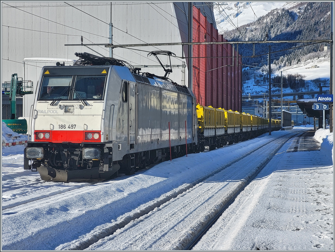 Die Railpool 186 497 ist mit ihrem aus Sggrrs S 204 Wagen bestehenden Ganz-Gterzug in Airolo angekommen. Die Wagen werden in der Folge unter die Beladungseinrichtung (links im Bild) rangiert und beladen. 

21. Jan. 2025