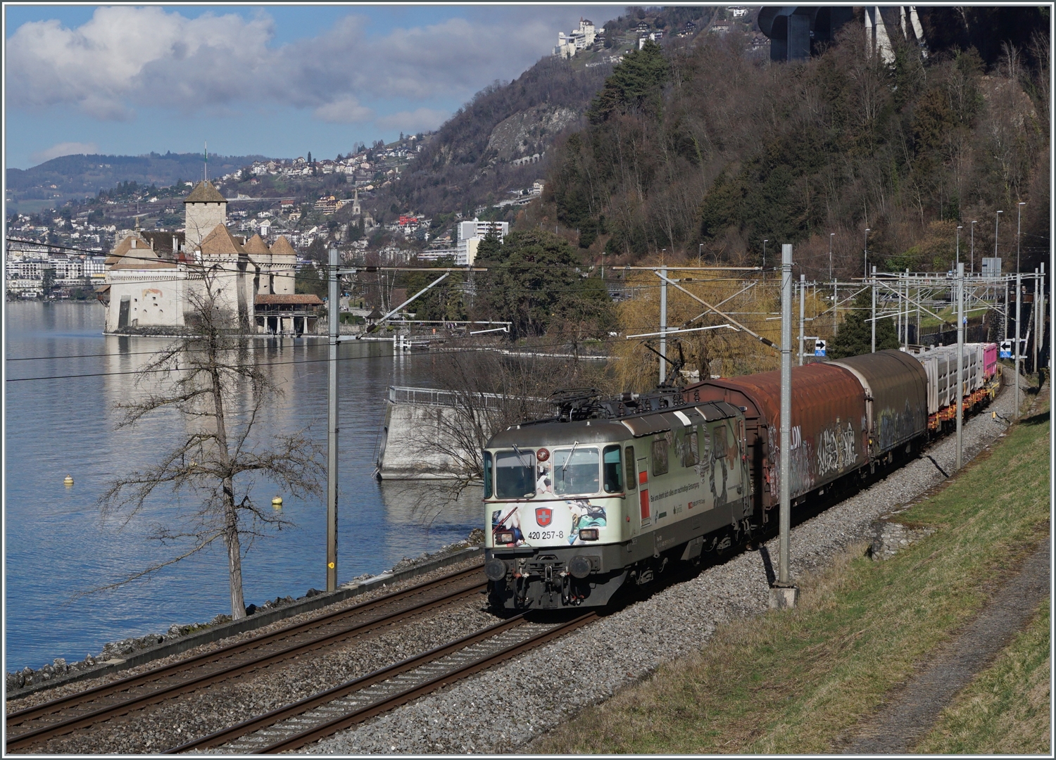 Die SBB Re 4/4 II 11275 (Re 420 257-8) mit einem Werbeanstrich ist mit einem Güterzug Richtung Wallis kurz vor Villeneuve unterwegs. Im Hintergrund das Château de Chillon.

13. Februar 2024
