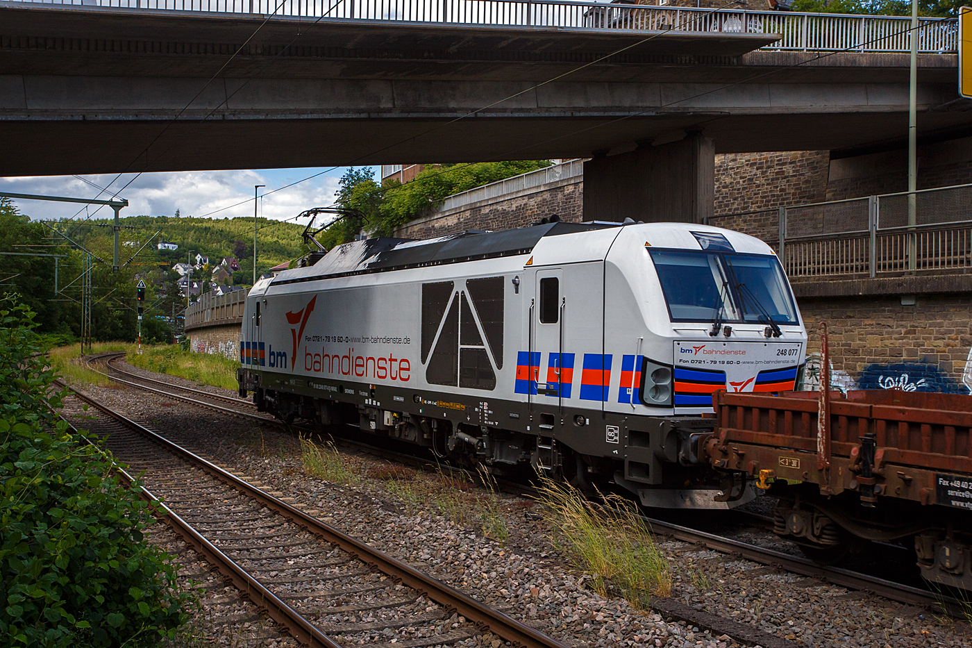 Die SIEMENS Vectron Dual Mode 248 077 (90 80 2248 077-0 D-NRAIL) der BM-Bahndienste GmbH (Karlsruhe) f�hrt am 09 Juni 2026, mit einem Flachwagenzug (4 Drehgestell-Flachwagen der Gattung Rens), durch den Bahnhof Kirchen/Sieg in Richtung Siegen.

Die SIEMENS Vectron DM wurde 2023 von Siemens Mobility GmbH in M�nchen-Allach unter der Fabriknummer 23425 und im Januar 2024 an die BM-Bahndienste GmbH ausgeliefert, die die Lok �ber die RRL - RIVE Rail Leasing Limited (Dublin) geleast hat, eingestellt wurde die Lok durch die northrail GmbH. 

Die Hybridlok (Vectron Dual Mode) kann die Antriebsenergie aus der Fahrleitung beziehen (2.400 kW Leistungen am Rad), oder mittels eines MTU 16V 4000 R84 V16-Zylinder-Dieselmotors (2.400 kW Motorleistung, 2.000 kW Leistungen am Rad) erzeugen.
