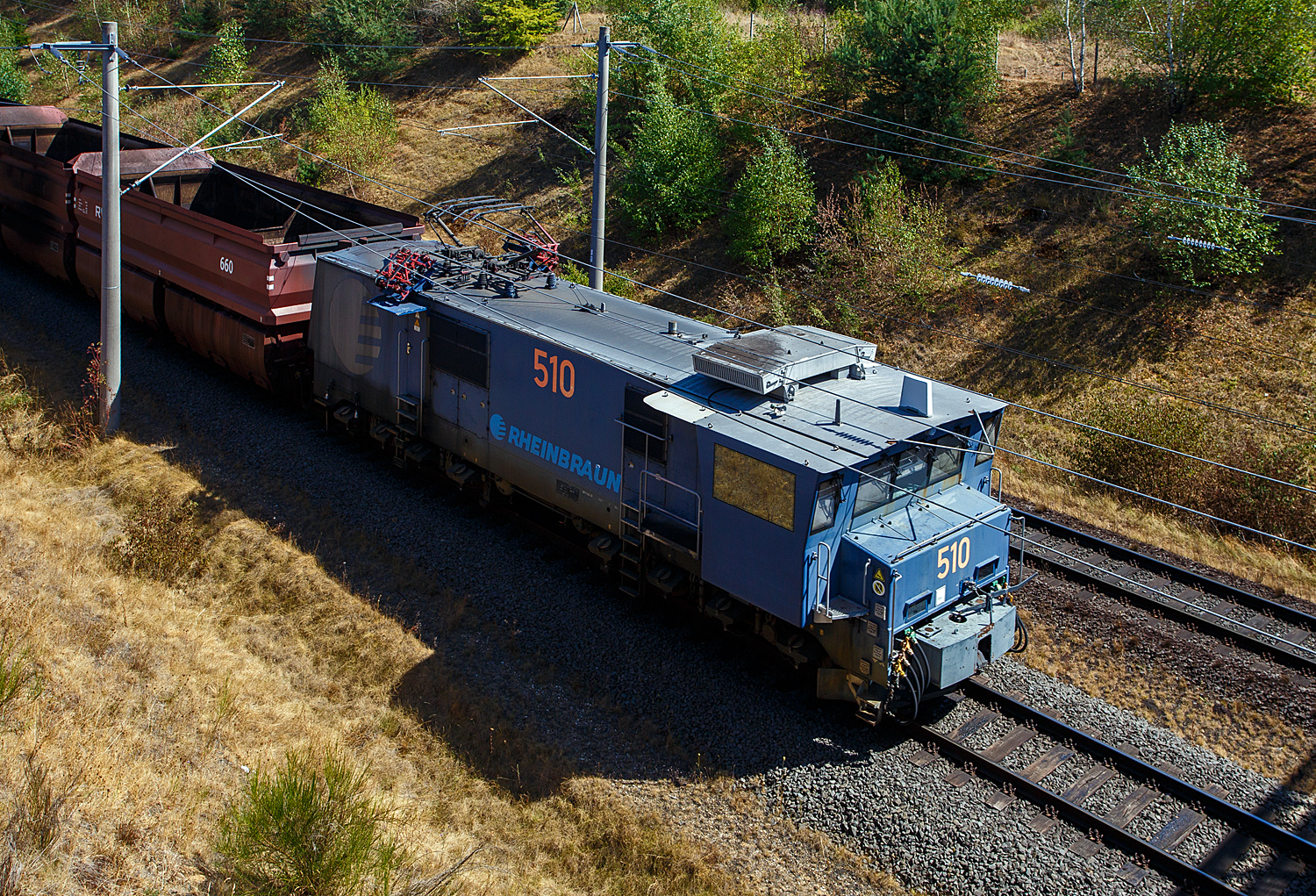 Die Tagebaulokomotive Adtranz - EL 2000 – 510 der RWE Power AG (ex Rheinbraun) kommt am 12 August 2026 bei Kerpen-Buir auf der Hambachbahn mit einen Braunkohle Selbstentladewagen Leerzug, von den Kraftwerken zum Tagebau Hambach.

Die RWE Power AG setzt zwei verschiedene Elektrolokomotiven ein - die zwischen 1954 und 1966 in gro�er St�ckzahl durch verschiedene Hersteller (Henschel, Krauss-Maffei und Krupp) gelieferte Type EL 1 (aktuell 21 Fahrzeuge im Einsatzbestand), sowie die 1999 - 2000 vom Kasseler ADtranz-Werk in einer St�ckzahl von zehn Maschinen gelieferte EL 2000. Die RWE Lok 510 wurde 2000 ADtranz (ABB Daimler Benz Transportation Adtranz) unter der Fabriknummer 33327 gebaut und an die Rheinbraun AG geliefert. Bei RWE Power hat sie zudem die Equip-Nr. 40043.

Adtranz EL 2000 sind die etwas st�rkeren Nachfolger der EL 1 Lok, da diese in die Jahre gekommen waren (Bj1954 bis 1965), musste Ersatz beschafft werden. Die elektrischen Tagebaulokomotiven des Typs Adtranz EL 2000 sind typischerweise (wie auch die EL 1) mit einer robusten Mittelpufferkupplung mit breiter Aufschlagfl�che ausger�stet. Diese Spezialkupplung ist notwendig, um den harten Belastungen beim Verschieben schwerer Abraum- und Kohlez�ge im rheinischen Braunkohlerevier standzuhalten. Markant ist neben der Kupplung das seitlich �berkragende F�hrerhaus f�r eine bessere Streckensicht bei geschobenen Z�gen. Auch die vielen Sandbeh�lter, je Seite sind es 8 St�ck sind sehr auff�llig. Neben den zwei Einholmstromabnehmer (im Tandem), besitzen die Tagebauloks seitliche Stromabnehmer, diese werden an der Verladestation (Kohlebunker) ben�tigt, damit die Waggons ohne st�renden Fahrdraht beladen werden k�nnen.

Technik
Die Lokomotiven besitzen einen F�hrerstand auf einer Seite mit einem kleinen Vorbau davor. Der F�hrerstand ist �ber 1,3 m breiter als der Fahrzeugkasten. Dadurch kann die Lokomotiven auch im Betrieb mit dem Maschinenraum voran betrieben werden. Die der Fahrleitung entnommene Energie (6 kV 50 Hz) wird auf dem Fahrzeug in die f�r die Fahrmotoren (Typ: ABB 6 FRA 7072) geeigneten umgewandelt. Dies geschieht mittels Trafo, 4 QS-Steller, Spannungszwischenkreis und Wechselrichter. Die Fahrmotoren sind �hnlich denen der bekannten Doppel-Elektrolok „IORE“ der schwedischen Erzbahn LKAB Malmtrafik AB. Die Antriebsleistung von den Fahrmotoren wird jeweils �ber Tatzlager mit einer �bersetzung 6,266 : 1 auf die Antriebwellen (Radsatzwellen) �bertragen. Daher sind dann auch die gewaltigen Zugkr�fte m�glich. 

TECHNISCHE DATEN der Adtranz EL 2000:
Gebaute Anzahl: 10 St�ck
Nummerierung: 501 bis 510
Spurweite: 1.435 mm (Normalspur)
Achsfolge: Bo'Bo'
L�nge �ber Puffer: 16.400 mm 
Drehzapfenabstand: 8.200 mm
Achsabstand im Drehgestell: 2.700 mm
Treibraddurchmesser: 1.250 mm (neu)
Breite: 4.500 mm
H�he: 4.075 mm (bei eingezogenem Stromabnehmer)
Eigengewicht: 140 t
Achslast: 35 t
H�chstgeschwindigkeit: 70 km/h
Stromsystem: 6 kV 50 Hz Einphasenwechselstrom
Dauerleistung: 2.800 kW
Anfahrzugkraft: 500 kN
Fahrmotoren: 4 St�ck (Typ: ABB 6 FRA 7072) / je 227 A / je 714 kW
Antriebart: �ber Tatzlager mit einer �bersetzung 6,266 : 1
Strom�bertragung: Oberleitung oder Seitenfahrleitung
Bremsen: Sab Wabco Druckluft-Klotzbremse, Federspeicher-Feststellbremse, Elektro-Bremse mit Stromr�ckspeisung in Fahrleitungsnetz. 
Sicherheitseinrichtungen: SIFA, magnetische Zugbeeinflussung (MZ), mech. Fahrwegsicherung (Druckluft-Bruchrohre), Druckluftpfeife und elektrisches L�utwerk.

Nochmals meinen Dank an Herrn Thomas Nie� der RWE Power AG f�r die Zusendung von Technischen Daten der Loks und Wagen. 

Der Eisenbahnbetrieb der RWE Power AG (ex Rheinbraun)
Auf einem 230 km langen Streckennetz, das auf den Hauptabfuhrstrecken f�r eine Achslast von 35 t ausgelegt ist, werden zu Spitzenzeiten die angeschlossenen Kraftwerke t�glich mit 220.000 – 230.000 t Kohle (das entspricht ungef�hr 170 Zugpaaren) versorgt. Allein das Kraftwerk Niederau�em verbraucht bis zu 90.000 t Kohle t�glich.

Der Eisenbahnbetrieb hat 270 Mitarbeiter, davon 180 Lokf�hrer. Bis zur Einstellung des Abraumbetriebes im Jahre 2001 standen f�r den Gesamtverkehr 54 Elektrolokomotiven zur Verf�gung. Aktuell stehen 31 Elektrolokomotiven im Einsatz. 17 Dieselloks sind vorrangig f�r Infrastrukturinstandhaltung im Einsatz. Daneben werden sie f�r �bergabefahrten in das �ffentliche Netz vorgehalten.

Es stehen 333 vierachsige Kohlewagen mit einem Gesamtgewicht ca. 120 t (bis 114 m�) und 140 achtachsige 96 m� Abraumwagen mit einer Tragf�higkeit von 180 t zur Verf�gung.

F�r Bereisungszwecke steht ein MAN-Schienenbus zur Verf�gung, der von der AKN stammt. Er erhielt von Nov. 2008 bis April 2010 in Delitzsch (EuroMaint) eine umfangreiche Aufarbeitung.


Hambachbahn
Die Hambachbahn ist eine Tagebau-Werksbahn der RWE Power (ex Rheinbraun) im Rheinischen Braunkohlerevier. Sie bindet den Tagebau Hambach an die Nord-S�d-Bahn an, �ber die die RWE-Kraftwerke in Niederau�em, Frimmersdorf und Neurath mit Braunkohle versorgt werden.

Die 1983 in Betrieb genommene Hambachbahn wird, wie auch die Nord-S�d-Bahn, elektrisch betrieben, jedoch als Besonderheit abweichend zum �blichen Bahnstrom mit Einphasenwechselstrom 6,6 kV und 50 Hz. 

Die Streckenl�nge in der Spurweite 1.435 mm (Normalspur), betr�gt 21,00 Kilometer. Die beginnt beim Kohlebunker Hambach (Verladestation) und endet beim Stellwerk Fn in Bergheim-Auenheim, wo sie dann an die Nord-S�d-Bahn anschlie�t. Im Bereich des Kohlenbunkers des Tagebaus Hambach befindet sich eine Wendeschleife.

Im Rahmen der Erweiterung des Tagebaus Hambach wurde der Streckenverlauf zusammen mit der Bundesautobahn 4 um etwa drei Kilometer nach S�den verlegt und beide verlaufen seit September 2014 parallel zur Schnellfahrstrecke K�ln–Aachen der Deutschen Bahn, es gibt jedoch keine direkte Verbindung zwischen den beiden Strecken. Die neue Strecke verl�uft aus Landschafts- und Schallschutzgr�nden in einem etwa 8 bis 15 Meter tiefen Einschnitt im Gel�nde. Aber im Gegensatz zur deutlich vernehmbaren DB Hauptstrecke und zum sehr lauten Rauschen der Autobahn n�hern sich die Braunkohlez�ge kaum h�rbar. 
