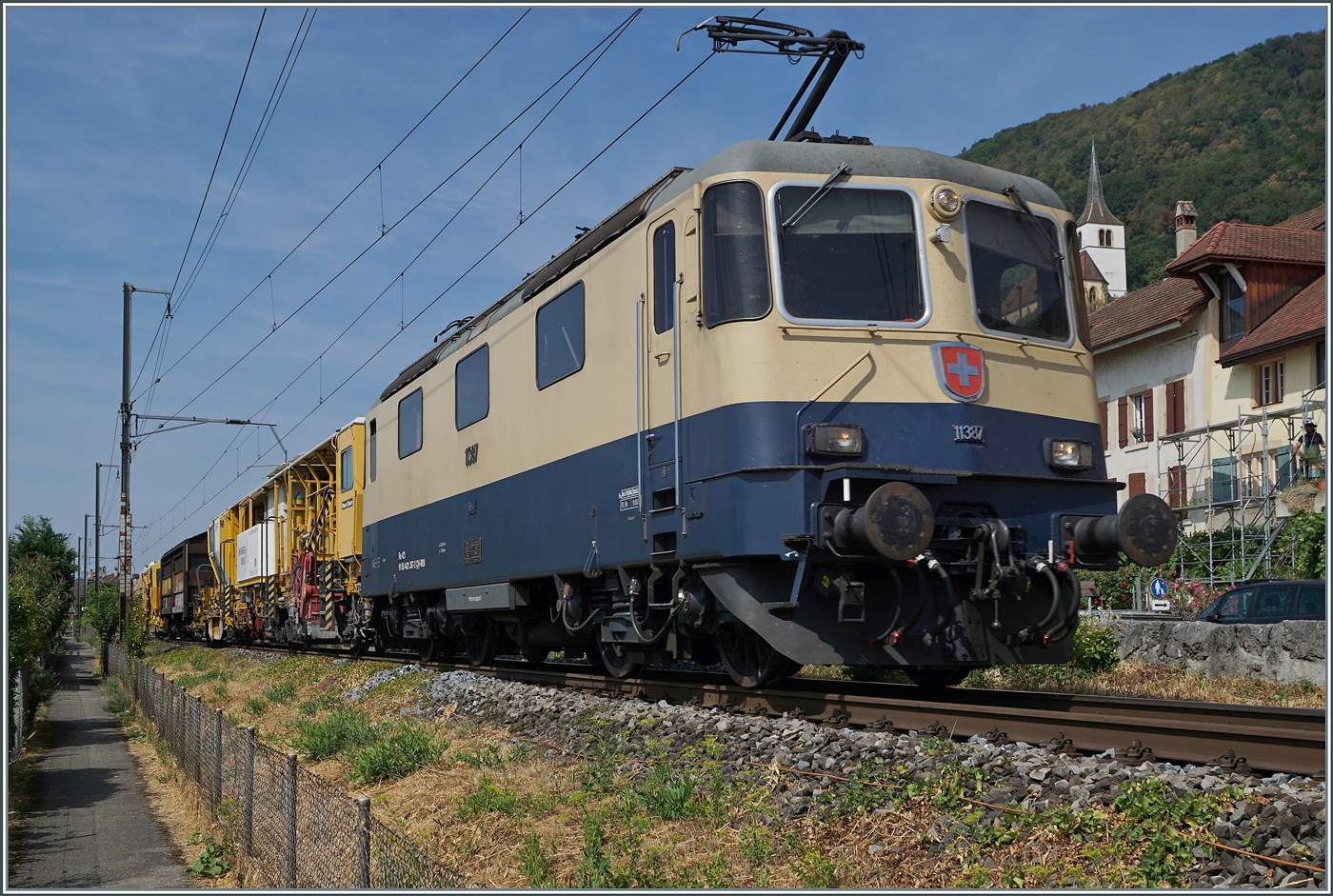Die �berrschung des Tages und dies gleich Bild f�llend: die IRSI  Rheingold  Re 4/4 II 11387 (Re 421 387-2 / UIC 91 85 4421 387-2 CH-IRSI) ist mit eine  gelben  Anhang in Ligerz auf dem Weg von Chavornay in Richtung Biel/Bienne. 
Obwohl die Lok das Bild sehr dominiert, ist doch noch der Kirchturm der bekannten Kirche von Ligerz zu sehen.  

16. Juli 2026