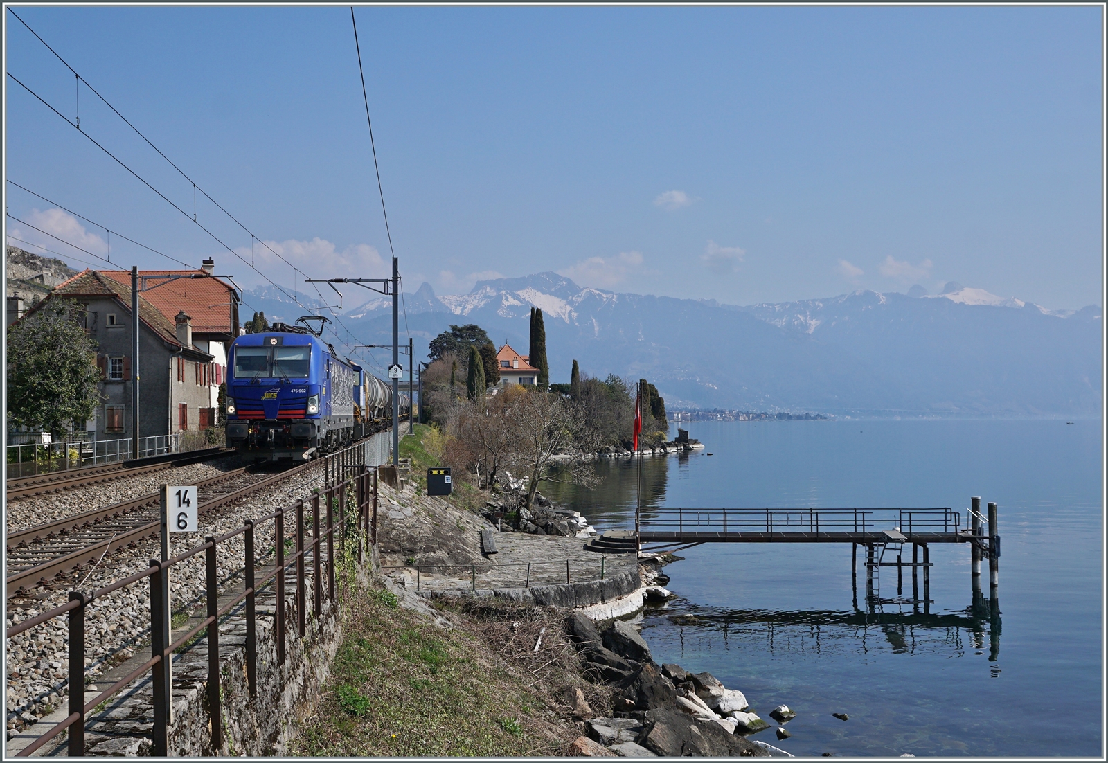 Die WRS Re 475 902 fährt mit einem Kesselwagenzug Richtung Lausanne bei St-Saphorin am Genfer See entlang. Das Bild entstand auf dem Bahnsteig von St-Saphorin.

25. März 2022 