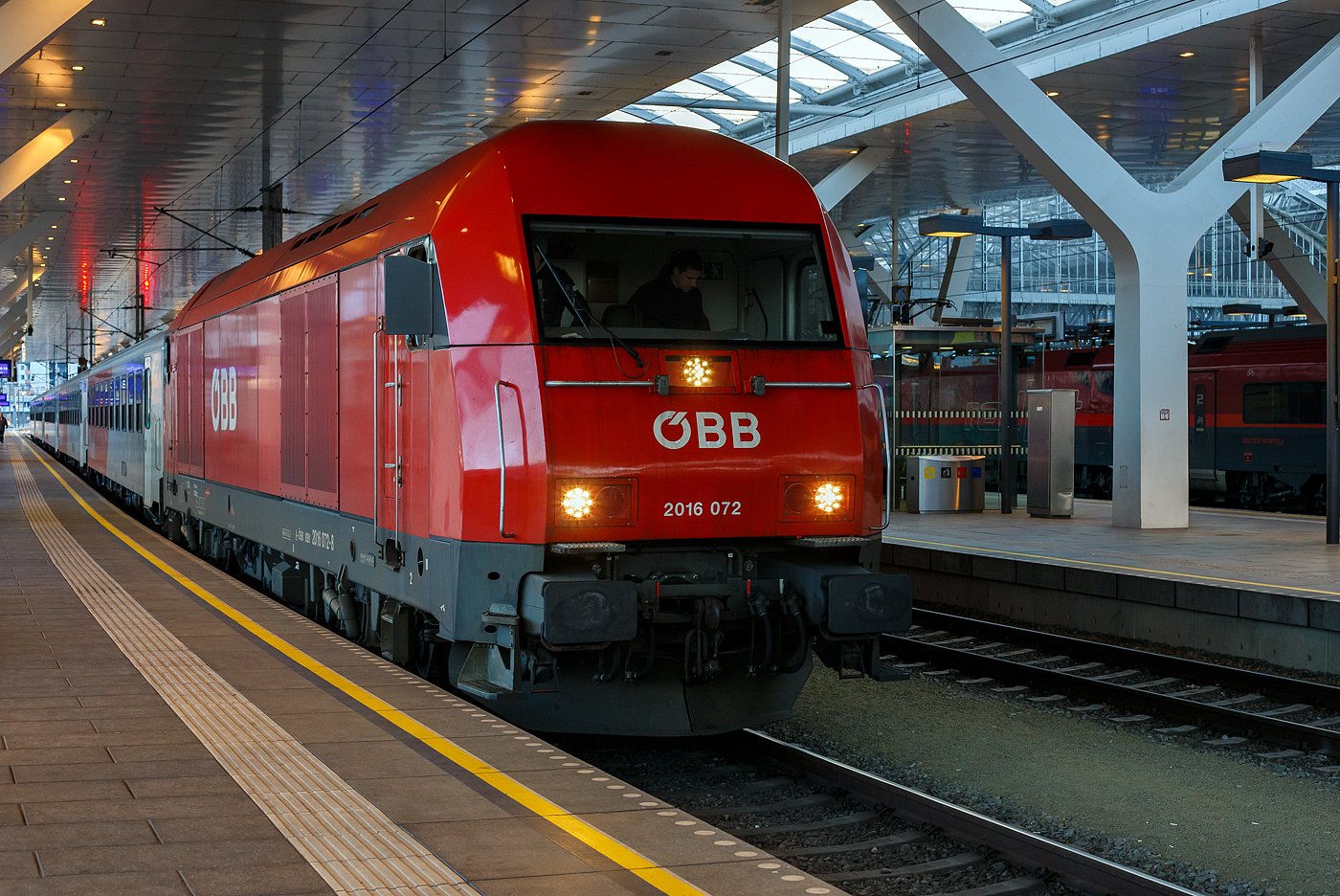 
Eine echte „Hercules“ die ÖBB 2016 072 (A-ÖBB 92 81 2016 072-8) am 13 Januar 2025, mit dem REX 21 (City Shuttle) von Salzburg Taxham über Neumarkt am Wallersee nach Braunau am Inn, beim Halt im Hauptbahnhof Salzburg. 

Die Siemens ER20 wurde 2004 von Siemens in München-Allach unter der Fabriknummer 20996 gebaut. Sie hat die Zulassungen für Österreich, Deutschland, Tschechien und die Slowakei. „Hercules“ ist ein Markenname der ÖBB für die Dieselelektrische Universallokomotive vom Typ Siemens ER20. 

Die Loks der Reihe 2016 der Österreichischen Bundesbahnen (ÖBB) sind vierachsige dieselelektrische Lokomotiven, die unter der Bezeichnung Hercules seit 2002 im Einsatz sind. Sie gehören der mittleren Leistungsklasse an und werden vor allen Zugarten eingesetzt. Auch der Verschub und Fahrverschub auf Dieselstrecken wird mittlerweile durch die 2016 geprägt.

Ende der 1990er Jahre wurde der Personen- und Güterverkehr auf den nicht elektrifizierten Strecken der Österreichischen Bundesbahnen (ÖBB) überwiegend mit Fahrzeugen aus den 1960er und 1970er Jahren betrieben. Zur Erneuerung der Fahrzeugflotte veröffentlichte die ÖBB 1997 eine Ausschreibung, um die Reihen 2043/2143 und 2050 zu ersetzen.

Der Auftrag über zunächst 40 Streckendiesellokomotiven wurde an Siemens AG, Österreich vergeben und in Verantwortung von Siemens Transport Systems, Erlangen konstruiert und gefertigt. 1999 wurde eine erste Option für 30 weitere Lokomotiven gezogen. Die erste Lokomotive wurde im Jahr Januar 2002 inbetriebgenommen. Später wurde eine Option über 30 weitere Lokomotiven gezogen.

Die Konstruktion der Reihe 2016 entspricht im Wesentlichen dem der ER20. Unterschiede gibt es nur bei einigen Ausstattungen, die speziell von der ÖBB gefordert wurden. Ein 2.000 Kilowatt leistender Dieselmotor mit angeflanschtem Drehstrom-Synchrongenerator erzeugt dabei den Strom für die vier Fahrmotoren (Einzelachsantrieb).

TECHNISCHE DATEN:
Hersteller: Siemens
Baujahre: 2002-2004
Gebaute Anzahl (Ordnungsnummer): 100 Stück (2016 001-100)
Achsformel: Bo’Bo’
Spurweite: 1.435 mm (Normalspur)
Länge über Puffer: 19.280 mm
Breite:  2.870 mm
Drehzapfenabstand: 10.360 mm
Achsabstand im Drehgestell:  2.700 mm
Raddurchmesser: 1.100 mm (neu) /1.020 mm (angenutzt)
Kleinster bef. Halbmesser: 100 m
Dienstmasse:  80 t
Höchstgeschwindigkeit: 140 km/h
Dieselmotorart: wassergekühlter viertakt-90°-V16-Zylinder-Dieselmotor mit Common-Rail-Einspritzung, Abgasturbolader und Ladeluftkühlung. Im Leerlauf werden zur Verbesserung der Abgaswerte 8 von 16 Zylindern abgeschaltet.
Motortyp:  MTU 16 V 4000 R41 (der MTU Friedrichshafen9
Motorhubraum: 76.265 cm³ (Bohrung × Hub = 170 mm × 210 mm)
Motorgewicht (trocken): ca. 9050 kg
Nenndrehzahl:  600 bis 1.800 U/min
Installierte Leistung:  2.000 kW (2.719 PS)
Anfahrzugkraft: 250 kN
Leistungsübertragung: dieselelektrisch (Drehstrom Generator - GTO Stromrichter und 4 Drehstrom Fahrmotore mit Ritzel-Hohlwellenantrieb)
Traktionsleistung (am Rad): 1.750 kW ohne ZS / 1.600 kW mit ZS
Tankinhalt:  2.800 l
Dynamisches Bremssystem Elektrodynamische Nutz- und Widerstandsbremse (Rückspeisung indie Zugsammelschiene bzw. für die Hilfsbetriebe je nach Möglichkeit)
Höchstleistung der dynamischen Bremse: 1.000 kN
Max. Bremskraft der dynamischen Bremse: 100 kN

Paradigmenwechsel. Wurden die ersten ÖBB-Diesellokomotiven nach dem zweiten Weltkrieg ausschließlich mit dieselelektrischer Kraftübertragung ausgerüstet, so entschied man sich damals aus Gründen der einfacheren Wartung und leichteren Instandhaltung für alle künftigen Diesellok Generationen für einen dieselhydraulischen Antrieb. Während bei ersterem ein oder mehrere Dieselmotoren Generatoren antreiben, die letztlich die Traktionsenergie für die Fahrmotoren erzeugen, treibt beim dieselhydraulischen Antrieb (vereinfacht gesagt) der Dieselmotor das Fahrzeug über ein Wendegetriebe an.

Jahrzehntelang wurden alle ÖBB-Dieselloks in dieser einfachen aber auch leistungstechnisch begrenzten Bauweise beschafft. Um die in die Jahre gekommenen Dieselloks der Reihen 2050, 2043 und 2143 zu ersetzen, wurde Ende der 1990er Jahre ein Projekt gestartet, das zum Inhalt die Erneuerung der Diesellokflotte hatte. Es sollten in drei Leistungskategorien über 200 Fahrzeuge beschafft und so für einen gehörigen Modernisierungsschub sorgen. Bei der neuen geplanten Streckendiesellok überlegte man sich erstmals seit über 40 Jahren wieder die Verwendung eines dieselelektrischen Antriebs.

Während des Bieterverfahrens kristallisierte sich heraus, dass doch nur zwei Kategorien von neuen Diesellokomotiven beschafft werden sollten. Nach der Endrunde wurde der Auftrag zur Lieferung der neuen Diesellok Generation an Siemens Transportation Systems vergeben. Hier konzentrieren wir uns auf die Streckendiesellok, des Siemens Baumusters ER 20 – ÖBB Reihe 2016.
Drehstromantrieb

Ein Novum nach so langer Zeit war die Verwendung eines dieselelektrischen Antriebs für die 2.000 kW starke Streckendiesellok. Der eingebaute MTU Motor treibt dabei einen Drehstromgenerator an, der vier, insgesamt rund 1.600 kW starke Drehstrommotoren mit dem elektrischen Traktionsstrom versorgt. Nach der griechischen Mythologie sollte die neue Streckendiesellokflotte der ÖBB den Namen „Hercules“ tragen. Ursprünglich war die Beschaffung von insgesamt 140 Lokomotiven geplant. Infolge der Änderung des Flottenmanagements und auch mangels Bedarf blieb es bei einer Bestellung von 100 Fahrzeugen, die den Bahnbetrieb auf nicht elektrifizierten Strecken in Österreich revolutionierten.

Sämtliche Fahrzeuge wurden bei Siemens TS in München-Allach (ehemals Krauss Maffei) gefertigt und beim ÖBB-Standort Wiener Neustadt in Betrieb genommen. Sofort nach der Betriebszulassung in Österreich gelangten die ÖBB-Hercules Loks zum Standort Graz, wo sie ab Mitte 2002 einen Großteil der Leistungen der damals dort eingesetzten 2143 übernahmen. Mit zunehmender Auslieferung wurden zuerst die Steiermark, dann auch zahlreiche Strecken in Niederösterreich auf die neue ÖBB-Reihe 2016 umgestellt. Besonders auf den dieselbetriebenen Steilstrecken können die Neubaufahrzeuge beweisen, was in ihnen steckt.
