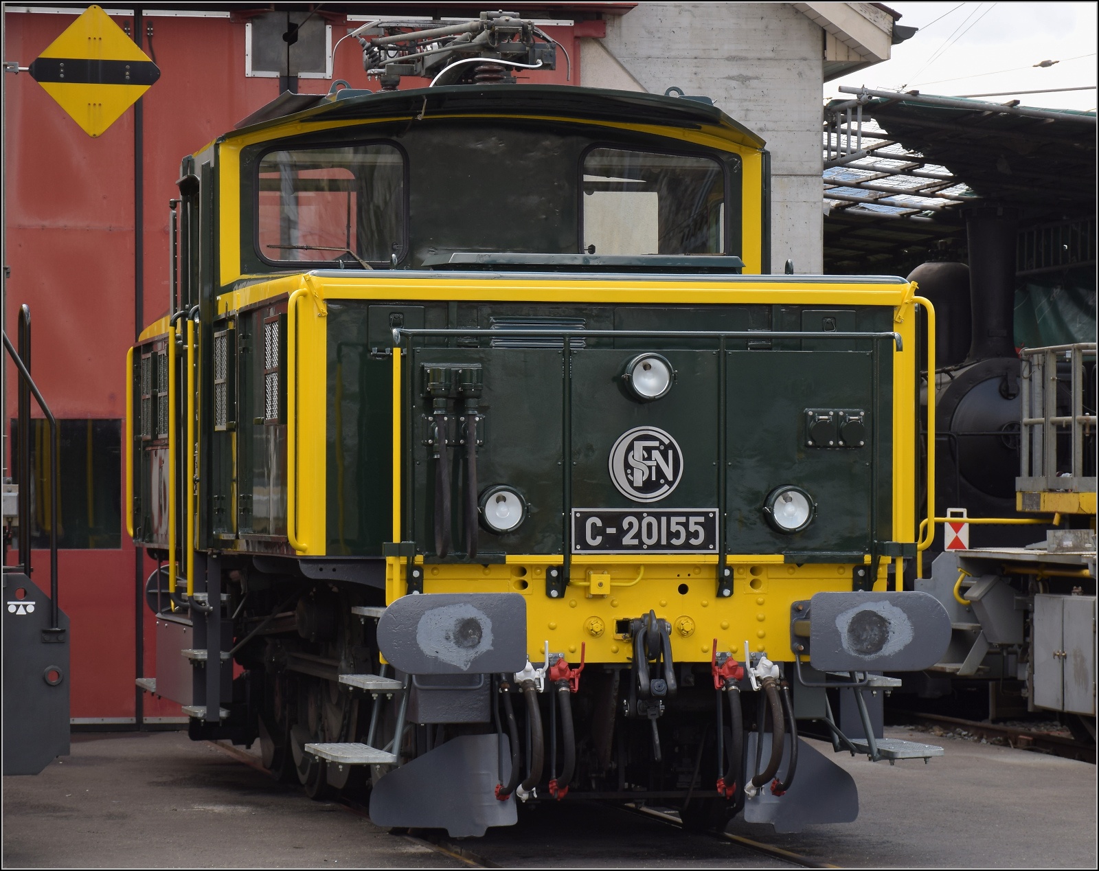 Etwas versteckt vor der Werkstatt in Balsthal steht die wunderbar in den Originalzustand zurückversetzte Zweispannungsrangierlok Ee 3/3 16515. Die letzte erhaltene Rangierlok dieser Baureihe war zu Beginn ihrer Karriere von den SNCF trotz sehr niedriger Höchstgeschwindigkeit im Streckendienst nach Basel eingesetzt. Weil sie doch im Rangierdienst besser geeignet ist, kam sie ein Jahrzehnt später zu den SBB als Ergänzung in den Rangierdienst. Ende letzten Jahres bekam sie ihr altes Farbkleid und die Bezeichnung C 20155 zurück. Nicht ganz unumstritten, aber meiner Meinung nach eine schöne Idee und wunderbar anzusehen. 

Dahinter steckt noch eine der kleinen Dampfloks der OeBB historic ihre Rauchkammertür an die frische Luft. Balsthal, April 2025. 