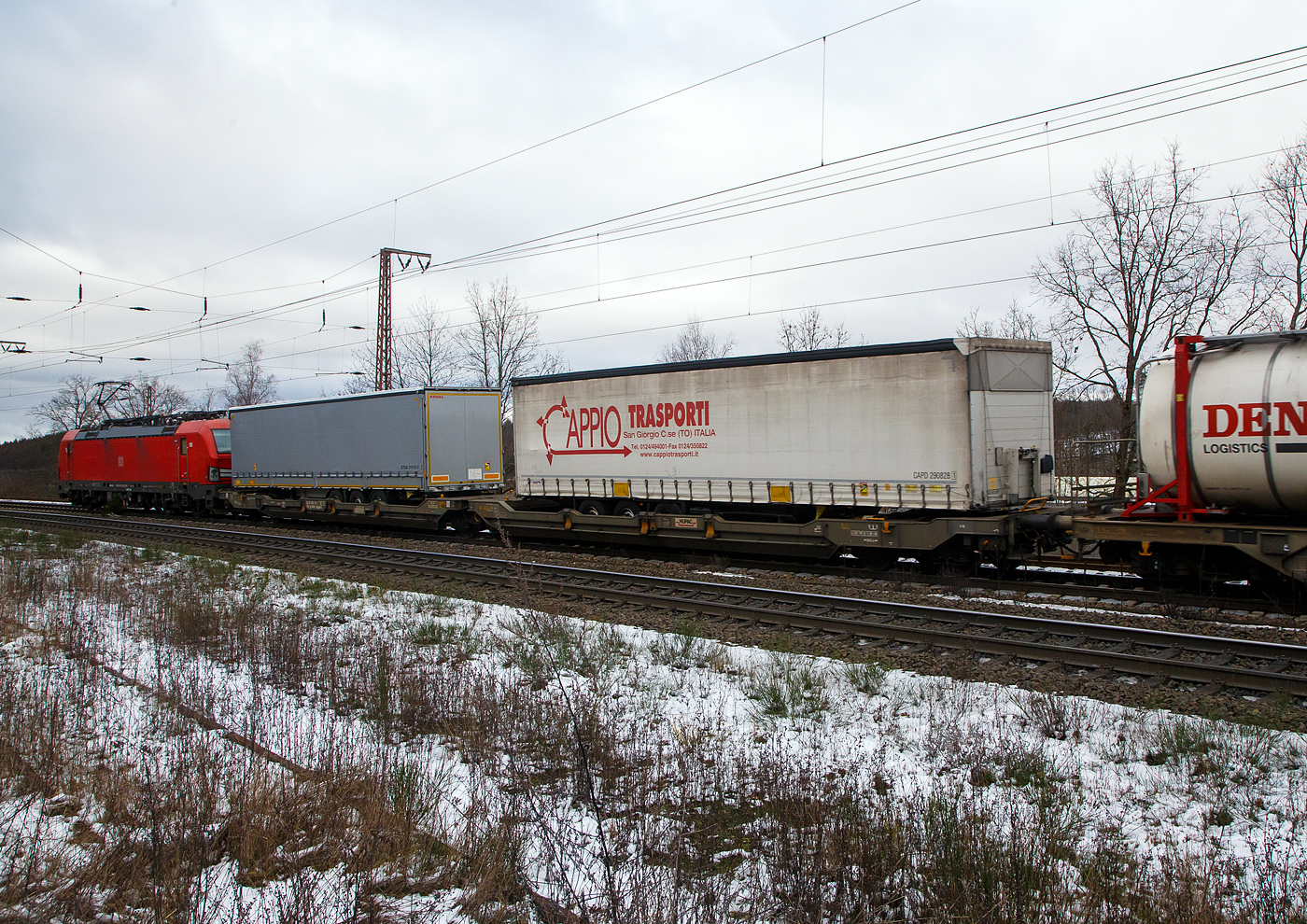 Hinter der DB 193 323-3....
Der sechsachsige Gelenk-Taschenwagen (Doppeltaschenwagen in Gelenkbauart), 33 85 4956 771-1 CH-HUPAC der Gattung Sdggmrss, der HUPAC Intermodal SA, am 27.01.2023 im Zugverband bei der Durchfahrt in Rudersdorf (Kr. Siegen), im Zugverband bei der Durchfahrt in Rudersdorf (Kr. Siegen), hier beladen mit zwei Sattelanhängern.

Diese Wagen vom Typ T5/T3000e wurde von Tatravagónka a.s. in Poprad (Slowakei) ab 2015 gebaut, die Entwicklung und auch Lizenzgeber ist die Ferriere Cattaneo SA in Giubiasco (Schweiz). Baugleiche Wagen sind auch bei anderen Halteren im Einsatz, die jeweils die Gattungskennzahl 4956 haben. Mögliche Ladeeinheiten sind zwei kranmanipulierbare Sattelauflieger oder alternativ bis zu vier Wechselbrücken und/oder Container. Dafür besitzt der Wagen einen dreifach verstellbaren Stützbock sowie für die Ladungseinheiten feste und klappbare Aufsetzzapfen auf den Langträgern. Das maximale Zuladegewicht beträgt für Sattelauflieger 2 × 40 t; die Basishöhe liegt bei 270 mm über SO.

TECHNISCHE DATEN:
Spurweite: 1.435 mm
Länge über Puffer: 34.200 mm
Drehzapfenabstand: 2 x 14.200 mm
Achsabstand in den Drehgestellen: 1.800 mm
Laufraddurchmesser: 920 mm (neu) / 860 mm (abgenutzt)
Ladelänge: 2 × 16.185 mm
Eigengewicht: 36.200 kg
Max. Zuladung bei Lastgrenze S: 98,8 t (ab Streckenklasse D)
Max. Zuladung bei Lastgrenze SS: 83,8 t (ab Streckenklasse C)
Max. Geschwindigkeit: 100 km/h / bei Lastgrenze SS und leer 120 km/h
Kleinster  befahrbarer Kurvenradius: R 75 m (R 150 m im Zugverband)
Intern. Verwendungsfähigkeit: TEN – GE

Die Bedeutung der Gattungs- und Kennbuchstaben (hier  Sdggmrss):
S - Drehgestell-Flachwagen in Sonderbauart
d - für den Transport von Straßenfahrzeugen eingerichtet
gg - für den Transport von Containern über 60 Fuß eingerichtet
m - bei mit sechs o. mehr  Radsätzen Ladelänge 18 m bis unter 22 m
r - Gelenkwagen
ss - Höchstgeschwindigkeit (beladen) bis zu 120 km/h
