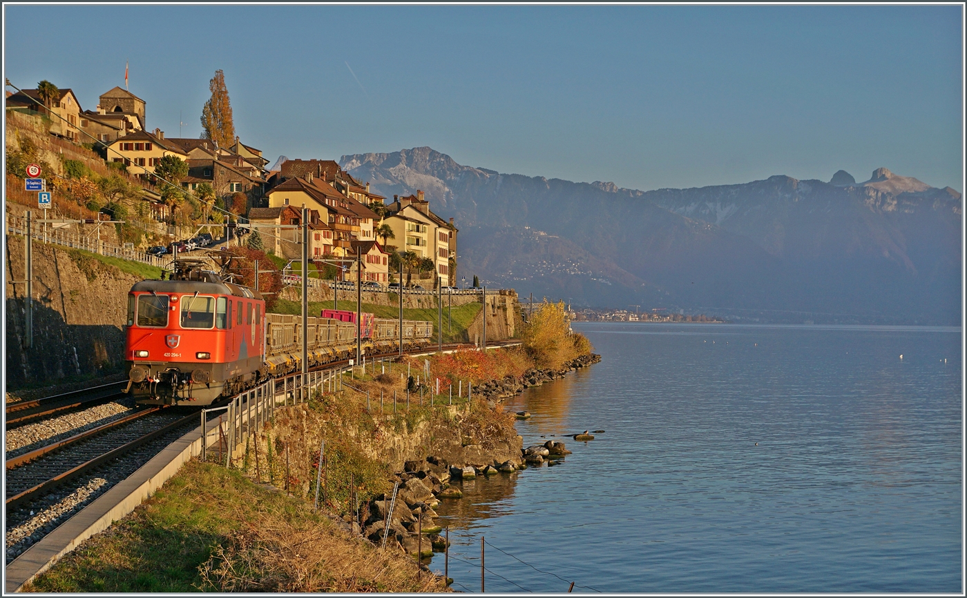 In der von der hinter meinem Rücken langsam untergehend Sonne schon etwas rot gefärbten Landschaft des Lavaux ist die SBB Re 4/4 II 11294 (Re 420 294-1)  100 Jahre Zirkus Knie  mit einem Güterzug auf dem Weg in Richtung Lausanne. 15. November 2024