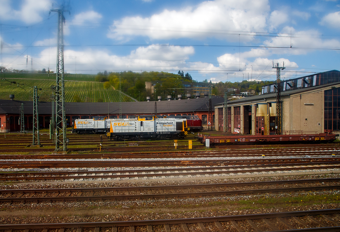 In Würzburg am 21 April 2023 aus einen aus einem fahrenden Zug durch die Scheibe fotografiert, bei den beiden Lokschuppen beim Hbf stehen:
Rechts der 8-achsiger Talbot-Niederflurwagen »Rollende Landstraße« (hier für den Bauzugdienst der DB), 81 80 4983 142-8 D-DBFWD der Gattung/Bauart Saadkms 690, der DB Fahrwegdienste GmbH.

Links im Vordergrund die V 150.04 (92 80 1293 510-4 D-SGL) der SGL - Schienen Güter Logistik GmbH, ex DB 710 966, ex DR110 966-9.

Dahinter links die V 180.13 (92 80 1203 158-1 D-SGL) der SGL - Schienen Güter Logistik GmbH, ex ALS 203 158-1, ex DB/DR 202 658-1, ex DR 112 658-0, ex DR 110 658-2. Vor dem Umbau zur BR 203.1 im Jahr 2007 durch ALSTOM Lokomotiven Service GmbH in Stendal, war die Lok, wie 7 Schwestermaschinen, von 2000 bis 2007 in der damaligen Provinz Kosovo der Bundesrepublik Jugoslawien (Savezna Republika Jugoslavija), ab 2003 Srbija i Crna Gora (Staatenbund Serbien und Montenegro), ab 2006 Republika Srbija (Republik Serbien). 5 Loks waren allerdings recht schnell defekt, weil man übersehen hatte, dass die Loks mangels Warmhaltemöglichkeit Frostschutz benötigen. Im Juni 2007 wurden die Lok von der PRESS - Eisenbahn-Bau- und Betriebsgesellschaft Pressnitztalbahn mbH in Jöhstadt nach Deutschland zurückgekauft. 

Dahinter rechts die V 270.10 „Detlef T.“ alias 221 124-1 (92 80 1 221 124-1 D-SGL) der SGL - Schienen Güter Logistik GmbH, ex PE 221 124-1 (Prignitzer Eisenbahn GmbH), ex ΟΣΕ A 419 (OSE- Organismós Sidirodrómon Elládos / griechische Eisenbahn), ex DB 221 124-1, ex DB V 200 124.
