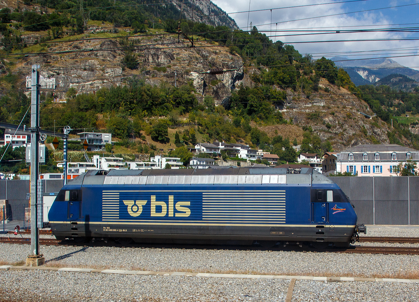 Noch im alten originalen Dunkelblau und somit noch nicht modernisiert, die BLS 465 002-4 „Görnergrat“ (91 85 4465 002-4 CH-BLS) seht am 08 September 2021 in Birg, aufgenommen aus einem IC.

Die BLS Re 465 stellen eine Weiterentwicklung der SBB Re 460 dar. Wie diese hat sie GTO-Thyristoren als Ventile im Stromrichter und Drehstrom-Asynchronmotoren. Der Unterschied liegt in der Umrichteranlage. Im Fall der Re 460 der SBB besteht ein Traktionsstromrichter (zwei je Lok, ein Gerät pro Drehgestell) aus zwei Vierquadrantenstellern die den Zwischenkreis parallel versorgen und einem Motor-Wechselrichter der zwei Motoren parallel speist. Die Stromrichter der BLS Re 465 gruppieren sich zu drei Vierquadrantenstellern parallel an einem Zwischenkreis mit zwei Wechselrichtern, je einen Motor im Drehgestell speisend. Somit lässt sich eine schleudernde Achse schneller und effektiver wieder in einen normalen Lauf bringen. Wurde bei der Entwicklung der Re 460 auf Dreipunkt-Stromrichter gesetzt, wurde im Gegensatz dazu die Re 465 mit Zweipunkt-Technik ausgestattet. Die Zwischenkreisspannung senkte man entsprechend von 3,5 kV (Re 460) auf 2,8 kV (Re 465). Zudem besitzt die Re 465 sechspolige Asynchron-Fahrmotoren, die Re 460 hingegen nur vierpolige Asynchronmotoren. Daraus resultiert eine gegenüber der Re 460 erhöhte Dauerleistung von 6.400 kW (Stundenleistung von 7000 kW). Die Radsätze im Drehgestell stellen sich radial zum Gleisbogen ein.

Zudem ist die Re 465 im Unterschied zur Re 460 mit der Vielfachsteuerung des Systems IIId und (mit Übergangskabel) BLS/BBC ausgerüstet. Dies erlaubt die Vielfachsteuerung zum Beispiel mit Re 4/4II, Re 4/4III, Re 6/6, Re 425 oder Ae 415.

In den Jahren 2019 bis 2022 wurden die Lokomotiven einem Refit unterzogen. Darin enthalten waren unter anderem der Einbau der Vielfachsteuerung ZMS für den Güterverkehr mit Traxx- und Vectron-Lokomotiven und ETB (Ethernet Train Backbone) für den Autoverlad am Lötschberg. Die Kästen wurden saniert und neu in hellem BLS-Lindengrün mit blauem Logo lackiert. Die Arbeiten wurden in der eigenen Werkstätte der BLS in Bönigen ausgeführt, die Kosten beliefen sich auf 20 Millionen Franken.