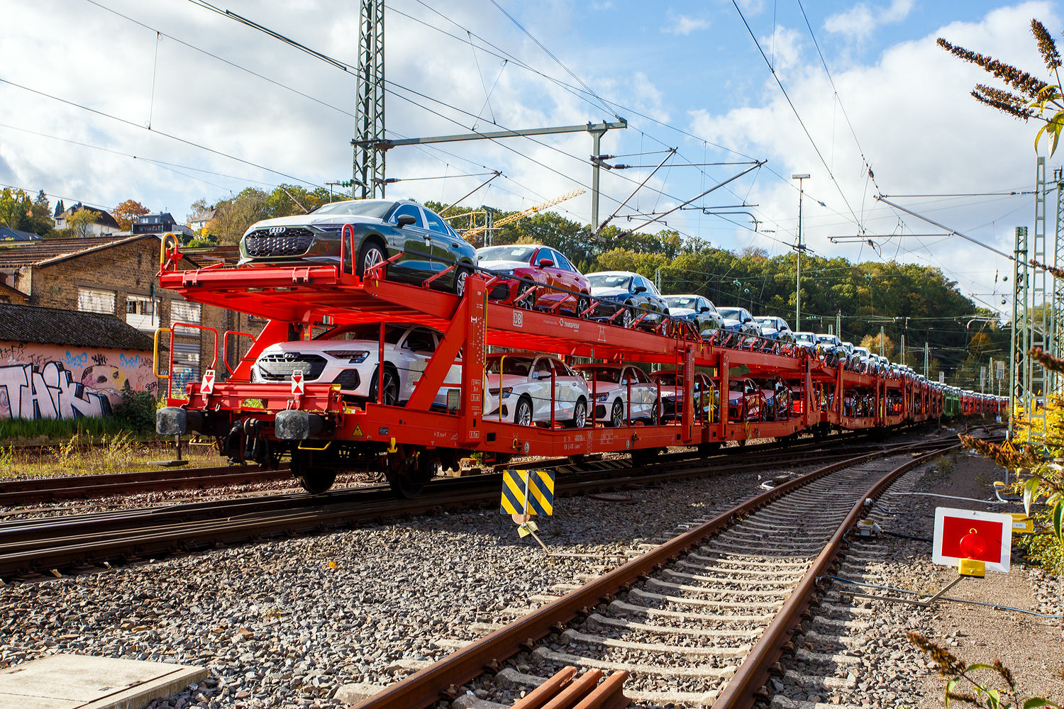 Vierachsiger (2 x zweiachsiger) Doppelstock-Autotransportwagen, 21 71 4363 036-6 E-ATG, der Gattung Laaers 560.2, der DB Cargo Logistics GmbH (ex DB Schenker ATG), am 24 Oktober 2026 im Zugverband, beladen mit Autos der bekannten Marke aus Ingolstadt, bei der Zugdurchfahrt in Betzdorf/Sieg in Richtung K�ln. 

Gebaut wurde der Wagen von der Tatravag�nka a.s. in Poprad (Slowakei). Der Wagen ist in Spanien eingestellt, an dem Wagen ist auch angeschrieben „DB in Korporation mit Transfesa. Die Transfesa Logistics S.A. ist ein spanisches Transport- und Logistik-Unternehmen mit Sitz in Madrid, das sich auf Schienen- und Stra�entransporte unter anderem f�r die Automobilindustrie spezialisiert hat. An Transfesa sind die Deutsche Bahn (ca. 84 %) und die Renfe (ca. 11 %) beteiligt. Der Rest ist im Streubesitz. Am 8. April 2026 wurde Transfesa Logistics offiziell in DB Cargo Iberia umbenannt, um die Pr�senz von DB Cargo in Spanien und im europ�ischen Schienennetz zu st�rken.

Die Autotransportwagen
Diese Waggons haben zwei Ladeebenen und sind f�r den europaweiten Transport geeignet. Sie werden f�r den internationalen Transport von PKWs, SUVs und Vans eingesetzt und bieten maximale Flexibilit�t durch eine stufenlos verstellbare obere Ladeebene. Aufgrund der hohen Lastgrenze (bis 34 t) ist der Transport von besonders schweren Fahrzeugen der genannten Typen m�glich.

Damit sowohl ein typenreiner Transport als auch eine Mischverladung in den unterschiedlichen Ladema�en m�glich ist, kann die obere Ladeebene hinsichtlich der Transportstellungen stufenlos eingestellt werden.

Durch die Entwicklung eines ver�nderten Ladungssicherungssystems wurde den Kundenanforderungen nach optimierten Transportm�glichkeiten f�r Fahrzeuge mit niedrigerer Bodenfreiheit Rechnung getragen.

Der gro�e Unterschied zwischen den Laaers-Wagen der Bauart 560.2 (wie hier) und der Bauart 560.1 sind das Lastgrenzenraster (Max. Zuladung), zudem ist die Bauart 560.2 meist 500 kg leichter.  

TECHNISCHE DATEN:
Gattung: Laaers (Bauart 560.2)
Erstes Baujahr der Wagengattung: 2007
Spurweite: 1.435 mm (Normalspur)
Anzahl der Achsen: 4 (2 x 2)
L�nge �ber Puffer: 31.000 mm
Achsabst�nde: 10.000 mm / 5.160 mm / 10.000 mm
Laufraddurchmesser (neu): �u�ere 840 mm und mittlere 730 mm
Ladel�nge: 30.070 mm (unten) / 30.550 mm (oben)
Ladel�nge waagerechter Teil untere Ebene: 19.400 mm
Ladebreite: 2.950 (unten) / 2.750 mm (oben)
H�chstgeschwindigkeit: 100 km/h (120 km/h leer)
Eigengewicht: 31.000 kg
Max. Zuladung bei Lastgrenze S: 33,0 t ab Streckenklasse B, bei Streckenklasse A 30,0 t
Max. Zuladung der Ladeebenen: unten und oben jeweils max. 18 t
Max. Gewicht je Pkw: 2.800 kg (Radlast max. 1 t)
Anzahl der Radvorleger: 64
H�he Gel�nder oben: 600 mm
Kleinster befahrb. Gleisbogenhalbmesser: 75 m
Bremse: KE-GP-A (K)
Bremssohle: Jurid 816 M
Handbremse: Ja
Intern. Verwendungsf�higkeit: TEN-GE