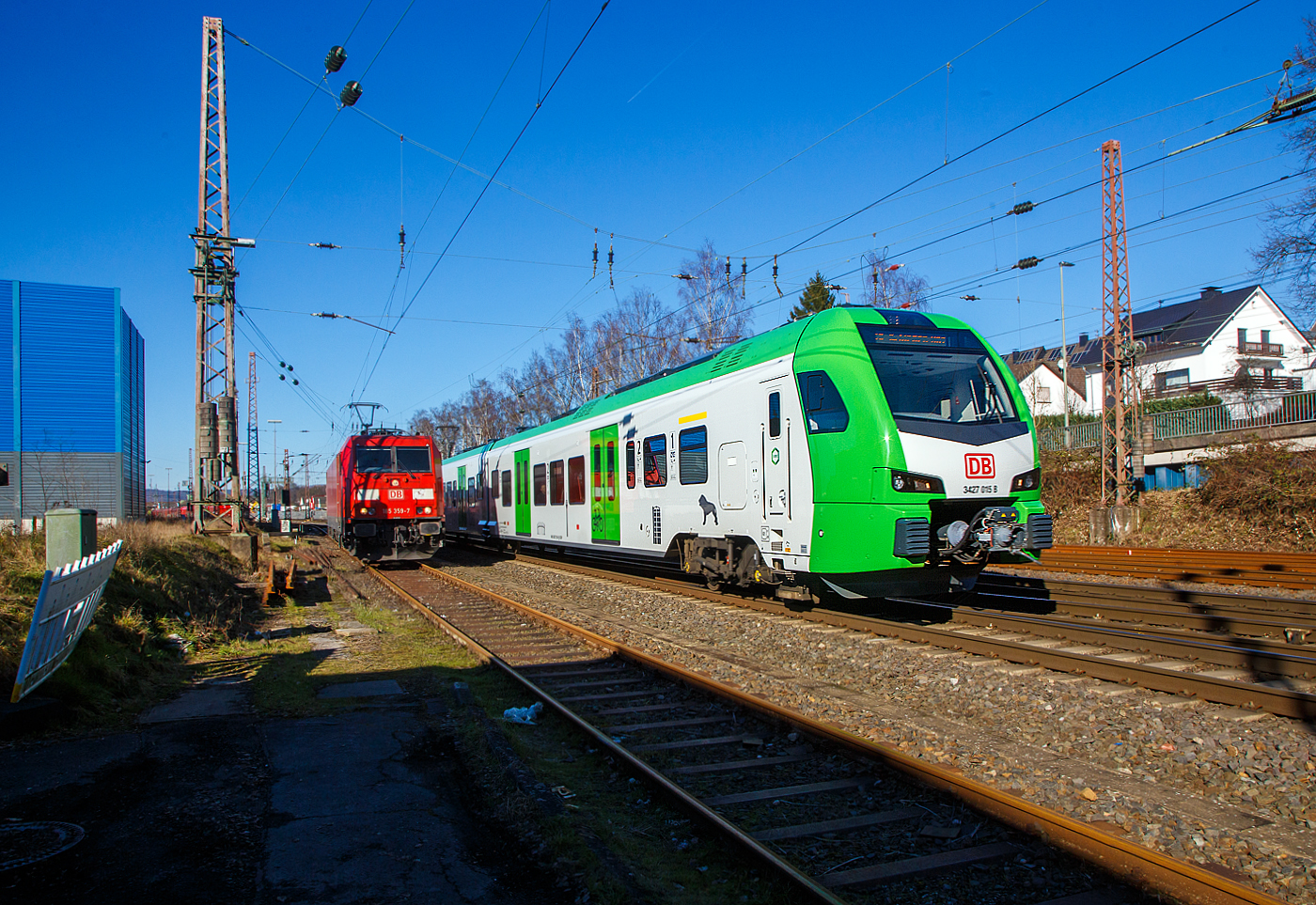 Während links auf dem Stumpfgleis die 185 359-7 der DB Cargo AG wartet, rauscht rechts der für die DB Regio AG – NRW fahrende dreiteilige Stadler FLIRT 3 XL 3427 015 (94 80 3427 015-7 D-STAP /  94 80 3827 015-3 D-STAP / 94 80 3427 515-6 D-STAP) der ZV VRR Eigenbetrieb Fahrzeuge und Infrastruktur, als RE 34 „Dortmund-Siegerland-Express“ (Dortmund - Letmathe - Siegen), von Kreuztal weiter in Richtung Siegen.

Der Stadler FLIRT 3 XL wurde 2020 von der Stadler Pankow GmbH in Berlin unter den Fabriknummern 42359 bis 42361 gebaut und an den Zweckverband Verkehrsverbund Rhein-Ruhr Eigenbetrieb Fahrzeuge und Infrastruktur geliefert. Eigentlich war dieser FLIRT 3 XL wie 9 weitere für die Bedienung der Regiobahnstrecke S 28 Kaarst - Neuss - Düsseldorf - Mettmann - Wuppertal vorgesehen, wo die Elektrifizierung bis 2020 erfolgen sollte. Da aufgrund von Verzögerungen der elektrische Betrieb voraussichtlich erst 2026 aufgenommen werden kann, wurden die inzwischen gelieferten Triebwagen u. a. von der DB Regio AG NRW eingesetzt.