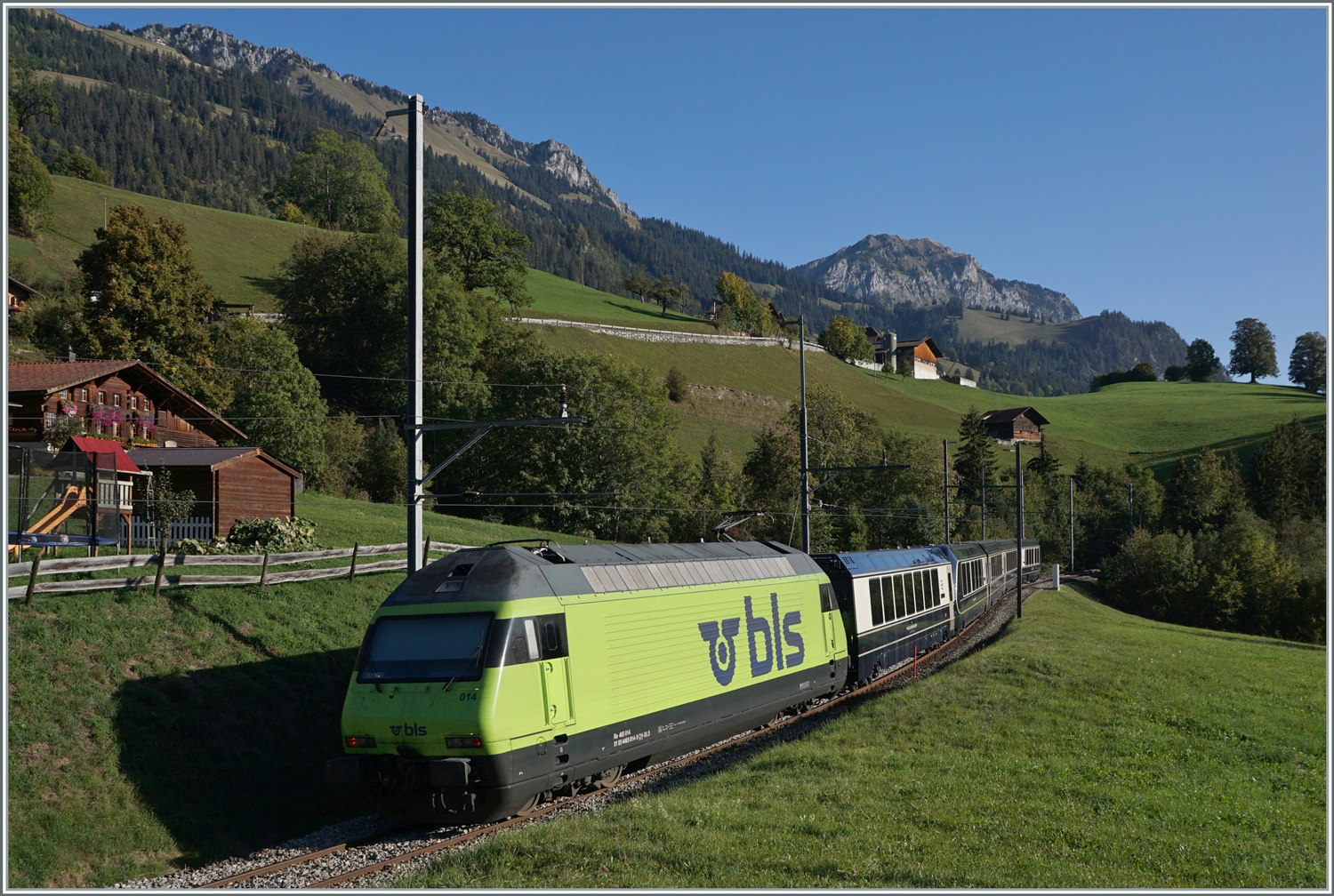 Weitaus besser zu sehen: die BLS Re 465 014 (UIC 91 85 4465 014-9) ist kurz nach der Haltestelle Enge im Simmental, welche der Zug ohne Halt passiert hat, mit dem GoldenPass Express GPX 4064 von Montreux nach Interlaken Ost unterwegs.

7. Okt. 2023