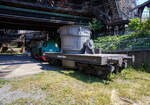 Ein vierachsiger normalspuriger offener Roheisenpfannenwagen der Burbacher Hütte hinter der Normalspur-Dampflokomotive 46, einer Jung Hochofenlok niedriger Bauart, der Völklinger Hütte (ehem. Röchling'schen Eisen- und Stahlwerke GmbH in Völklingen/Saar, ab 1982 ARBED-Saarstahl GmbH, ab 1986 Saarstahl Völklingen GmbH), ausgestellt als Denkmal am Gelände Völklinger Hütte, hier am 01 Juli 2025 am Gelände Völklinger Hütte als Denkmal. Heutiger Eigentümer ist die Initiative Völklinger Hütte e.V..

1971 fusionierten die Burbacher und Völklinger Hütte, und ab 1975 wurde die Stahlproduktion in der Burbacher Hütte eingestellt. Das Bild zeigt einen offenen Pfannenwagen, mit dem das flüssige und heiße Roheisen aus dem Hochofen aufgefangen wird, und dann zur Weiterverarbeitung mittels Werkseisenbahn zur Weiterverarbeitung in das angrenzende Stahl- und Walzwerk weitertransportiert wurde. Da die Entfernungen gering waren, benötigte man keine mit Schamott ausgemauerten Torpedopfannenwagen. Ob der Wagen hier auf der Völklinger Hütte ist mit nicht klar, aber da er erheblich höher ist als die Lok, so vermute ich das er hier keinen Einsatz fand.