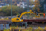 Ein LIEBHERR Zweiwegebagger A 922 Rail Litronic der SPITZKE SE (Großbeeren) mit angebautem Schwellenverlegegerät Typ 159-5 greift sich die nächsten 5 Schwellen von einem Res-Güterwagen und verlegt diese im neuen Gleisbett im Rbf Betzdorf/Sieg am 08. November 2025. Hier werden zurzeit Gleise erneuert.