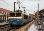 Die SNCF BB 22312  Antibes / Juan-les-Pins  (BB 5 22312R bzw. UIC: F-SNCF 91 87 0022 312-) hat am 25 M�rz.2015 mit einem TER Regionalzug den Bahnhof Marseille-Saint-Charles erreicht. Es regnete Bindf�den. 

An Hand der ersten Ziffer vor der Loknummer (5), kann man die die Zugeh�rigkeit zum Gesch�ftsbereich der SNCF erkennen, die  5  steht f�r TER (Regionalverkehr). 
Mit der Aufgliederung der SNCF in verschiedene Gesch�ftsbereiche wurde der Bestand an Loks zum 1. Januar 1999 aufgeteilt, die Zugeh�rigkeit kann man an der ersten Ziffer erkennen:
1 = VFE (Fernverkehr),
2 = CIC (�berregionaler Personenverkehr),
4 = Fret (G�terverkehr) und
5 = TER (Regionalverkehr).

Das  R  hinter der Loknummer zeigt dass diese Lok Wendezugtauglich ist. Ab 2006 wurden einige BB 22200 mit Wendezugsteuerungen versehen, zur Kennzeichnung, wurde wie bei dieser, der Loknummer das  R  (R = r�versible) nachgesetzt. 

Die Lok BB 22312 tr�gt das Wappen der franz�sischen Stadt Antibes / Juan-les-Pins, diese liegt an der Eisenbahnstrecke von Marseille nach Monaco (zwischen Cannes und Nizza) an der C�te d’Azu. Juan-les-Pins ist ein Seebad an der C�te d’Azur. Der Ort geh�rt zur Gemeinde Antibes und liegt im D�partement Alpes-Maritimes in der R�gion Provence-Alpes-C�te.

Die BB 22200 ist eine Zweisystemlokomotive f�r den Einsatz sowohl auf dem mit 1,5 kV elektrifizierten Gleichstromnetz der SNCF als auch auf dem mit 25 kV 50 Hz elektrifizierten Wechselstromnetz. In den Jahren 1976 bis 1986 wurden von Alsthom in sechs Bauserien insgesamt 205 Lokomotiven gebaut.

In den 1970er-Jahren ben�tigte die SNCF neue Mehrsystemlokomotiven, um unter beiden Stromsystemen ohne Lokwechsel fahren zu k�nnen. Aus der ab 1971 gelieferten Baureihe BB 15000 und der ab 1976 gebauten Gleichstrombaureihe BB 7200 wurde die BB 22200 als Mehrsystemvariante entwickelt. Die Baureihenbezeichnung bildet die Summe aus denen der beiden Schwesterbauarten.

TECHNISCHE DATEN:
Gebaute St�ckzahl: 205
Hersteller: Alstom
Baujahre: 1976–1986
Spurweite: 1.435 mm (Normalspur)
Achsformel: B'B'
L�nge �ber Puffer: 17.480 mm
Drehzapfenabstand: 9.694 mm
Achsabstand im Drehgestell: 2.800 mm
Triebraddurchmesser (neu): 1.250 mm
Dienstgewicht: 90 t
H�chstgeschwindigkeit: 160 km/h (wenige umgebaute 200 km/h)
Dauerleistung: 4.140 kW (bei 25 kV 50 Hz) / 4.040 kW (bei 1,5 kV CC)
Stromsystem: 25 kV/50 Hz AC, 1,5 kV DC
Anzahl der Fahrmotoren: 2 (TAB 674)