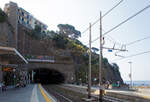 Der Cinque Terre Bahnhof Riomaggiore an der Bahnstrecke Pisa–Genua (RFI Strecke-Nr. 77 / KBS 31 La Spezia–Genua) am 22.07.2022. Hier mit Blick auf den südlichen Tunnel (in Richtung La Spezia), links vom Signal hinter den Tafeln ist der Eingang zu dem durch den Eisenbahntunnel verlaufenden Fußpfad zum Ortskern. Wiederrum links davon der hohe Lift (Aufzug), mit diesem kommt man auf den etliche Meter oben liegenden Weg. Der Lift ist aber in der Saison kostenpflichtig, er erspart einem aber etliche Treppenstufen oder einen gewaltigen Umweg.