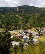 Ganz so schlimm (aus der Ferne), wie Stefan es beschreibt, finde ich es nicht.
Blick auf den neuen ÖV-Hub Fiesch am 07 September 2021 aus einem MGB-Zug. Ein Jahrhundertbau in Fiesch, MGB Bahnhof (1.063 m ü.M.) und Bus-Terminal mit dem direkten Zugang zur Talstation der neuen 10er-Kabinenbahn der Doppelmayr/Garaventa-Gruppe hinauf auf die Fiescheralp. 

Die neue 10er-Gondelbahn Fiesch - Fiescheralp / Kühboden, Baujahr 2019 von der Doppelmayr/Garaventa-Gruppe ist mit 7 m/s Fahrgeschwindigkeit die schnellste 10er-Gondelbahn der Schweiz. Sie ist eine sogenannte D-Line-Bahn der Doppelmayr/Garaventa-Gruppe mit Seillageüberwachung RPD. Als Betriebsmittel kommen die neuen CWA Kabinen Omega V zum Einsatz. Als Antrieb wurde der 867 kW starke Doppelmayr Sector Drive (DSD) verwendet, ein permanenterregter Synchronmotor, der mit modernster Frequenzumrichtertechnologie arbeitet und sich auch für steile Anlagen wie die hier in Fiesch sehr gut eignet.

Die neue Gondelbahn ersetzt zwei Pendelbahnen von Fiesch zur Fiescheralp, einmal mit 100er-Kabinen und einmal mit 34er-Kabinen. Die Talstation der hochmodernen Anlage befindet sich im neuen ÖV-Hub (Knotenpunkt Öffentlicher Verkehr) in Fiesch, wo direkter Anschluss an die Matterhorn-Gotthard-Bahn und das Postautonetz besteht.

Ein Ausbau der Bahn mit einer zweiten Sektion vom Kühboden Richtung Eggishorn als Ersatz für die Luftseilbahn Fiesch-Eggishorn ist angedacht und bereits genehmigt.

Immer mehr Skitouristen nutzen den öffentlichen Verkehr für die Fahrt in den Wintersport. Voll diesem Trend entsprechend haben die Aletsch Bahnen, die Matterhorn-Gotthard-Bahn (MGB) und die Gemeinde Fiesch als Bauherren mit dem Architekten und Investor Hans Ritz die neue ÖV-Drehscheibe in Fiesch als Gemeinschaftsprojekt gebaut. Der neue Verkehrsknotenpunkt besteht aus der Talstation der neuen 10er-Kabinenbahn auf die Fiescheralp, einem komplett neuen Bahnhof der MGB und einem Postbus-Terminal. Durch die Integration und Verknüpfung aller Verkehrsträger an einem Ort wurden kurze, schnelle und barrierefreie Umsteigwege geschaffen.

Für das Projekt hat die MGB den Haltepunkt für ihre Züge vom bisherigen Bahnhofsgebäude 400 m nach Norden verlegt und in den ÖV-Hub integriert. Dadurch ist ein komplett neuer Bahnhof mit zwei Außenbahnsteigen sowie einem 600 m langen neuen Doppelgleis für eine optimierte Kreuzungsmöglichkeit der Züge entstanden. Eine besondere Herausforderung bei der Gleisverlegung stellte die 36 m lange Bogenweiche mit einem Gewicht von 35 t dar. Sie wurde in drei Teilen angeliefert und dann mit einem Kran über die Dächer gehievt und eingebaut.

Die neue Kabinenbahn ersetzte die 100er-Pendelbahn Fiesch – Fiescheralp (Kühboden) von Garaventa aus dem Jahr 1974. Für die neue Bergstation wurde die bestehende Bausubstanz der abgebauten Pendelbahn erweitert und für die Garagierung der Kabinen verwendet. Bei der Talstation wurden 760 m“ und bei der Bergstation 1.100 m² Kunststoff-Folie als Fassaden-verkleidung eingesetzt. Die Verkehrswege in den Stationen sind barrierefrei angelegt. Die Bahn ist mit der neuesten Kabinengeneration der Omega V von CWA ausgestattet, für den Gütertransport stehen zwei Transportkabinen zur Verfügung.

Der ÖV-Hub Fiesch wurde nach einer äußerst kurzen Bauzeit von 14 Monaten am 7. Dezember 2019 feierlich eröffnet. Mit rund 24 Mio. CHF übernahm die Aletsch Bahnen AG den Hauptanteil dieser Investition. Die MGB beteiligte sich mit 17,6 Mio. CHF, der Architekt Hans Ritz investierte 6 Mio. Das Vorzeigeprojekt ÖV-Hub Fiesch macht eindrucksvoll deutlich, was durch Kooperation von verschiedenen Partnern erreicht werden kann.

TECHNISCHE DATEN der Seilbahn:
Hersteller:  Garaventa  (Doppelmayr/Garaventa-Gruppe)
Typ: 10er Gondelbahn (Ein-Seil-Umlaufbahn)
Baujahr: 2019
Höhe der Talstation:1.083 m ü. M.
Höhe der Bergstation: 2.227 m ü. M.
Höhendifferenz: 1.144 m
Abstand zwischen Tal- und Bergstation: 2.698 m
Anzahl der Stützen: 15
Förderseildurchmesser: 56 mm
Antriebsstation: Berg (Spanneinrichtung Tal)
Motorleistung: 867 kW (im Betrieb) / 1.124 kW (beim Anfahren)
Geschwindigkeit:  7 Meter pro Sekunde
Effektive Fahrzeit: 7:48 Minuten
Förderleistung: 1.880 Personen pro Stunde
Kabinenanzahl: 48 und 2 Transport-/Güterkabinen
Kabinentyp: CWA Omega V
