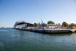 Blick am 15 Mai 2022 von der Fähre Warnemünde  - Hohe Düne der Weiße Flotte GmbH auf das Warnemünder Passagierkai, Pier 7 hinten das Warnemünde Cruise Center und dahinter am Pier 8, das gewaltige Kreuzfahrtschiff Norwegian Getaway. Rechts noch das Pier7 ein Shop und SB Restaurant mit Biergarten, davor (ganz rechts) mit einer Sand-Skulptur als Werbung für die 12. Warnemünder Sandwelt.